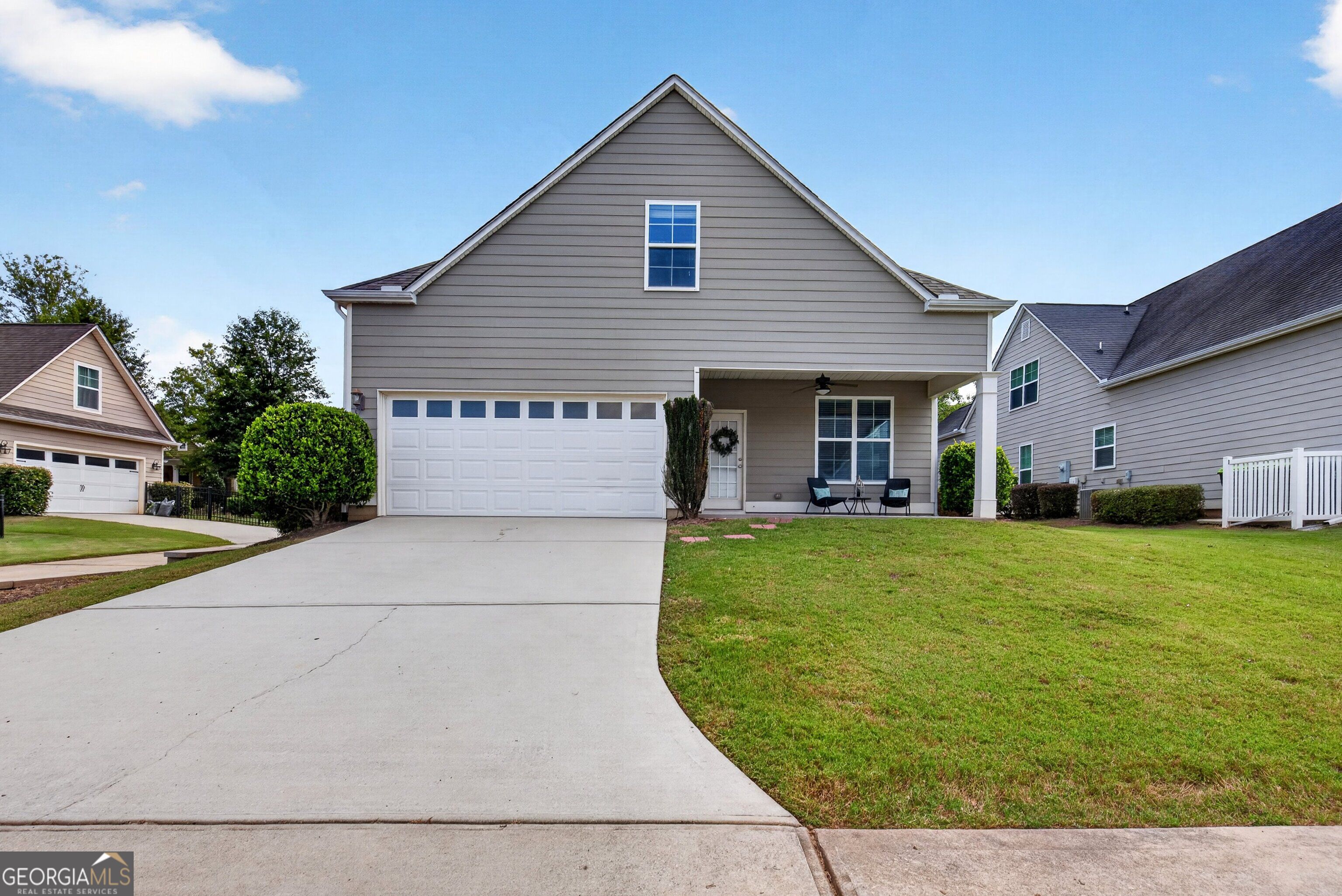 Gray two-story house with a steep gable, double garage, covered porch, and broad concrete driveway.