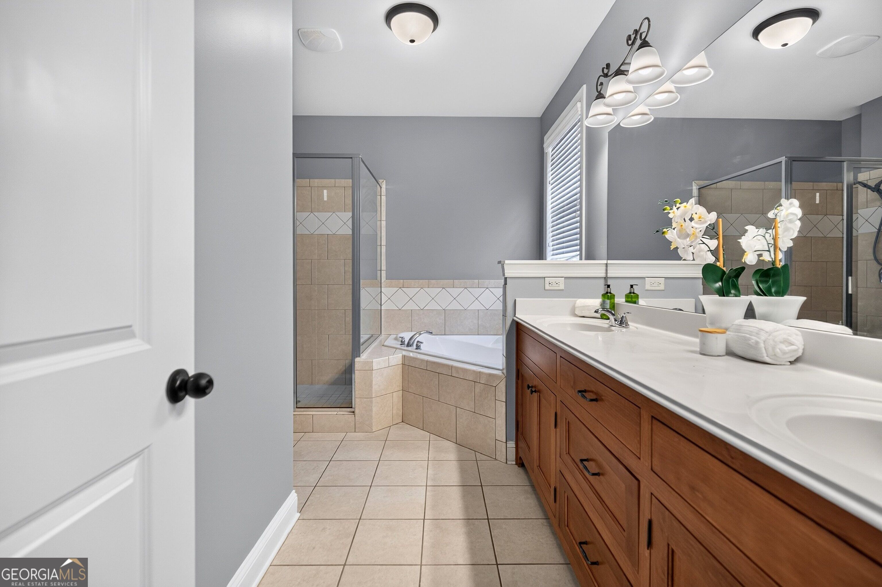 Bathroom with a long double-sink vanity, wood cabinets, corner bathtub, and glass-enclosed shower.