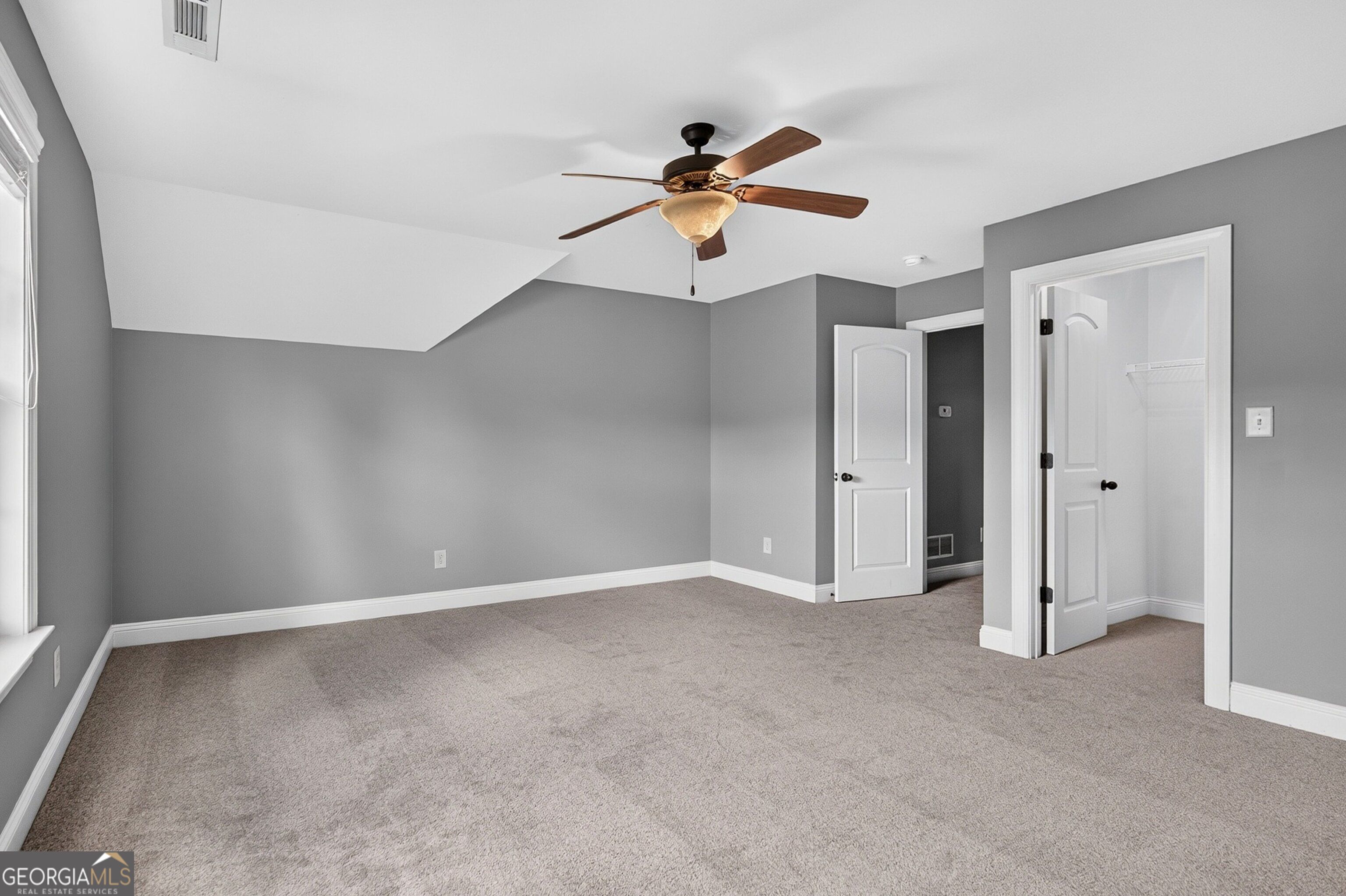 Empty bedroom with gray walls, beige carpet, a ceiling fan, and two open white doors.