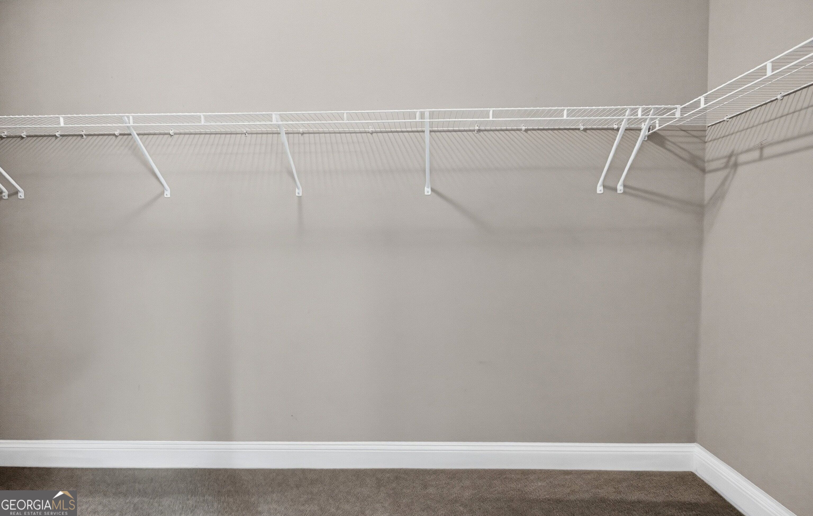 Empty walk-in closet with white wire shelving and hanging rods along three walls.