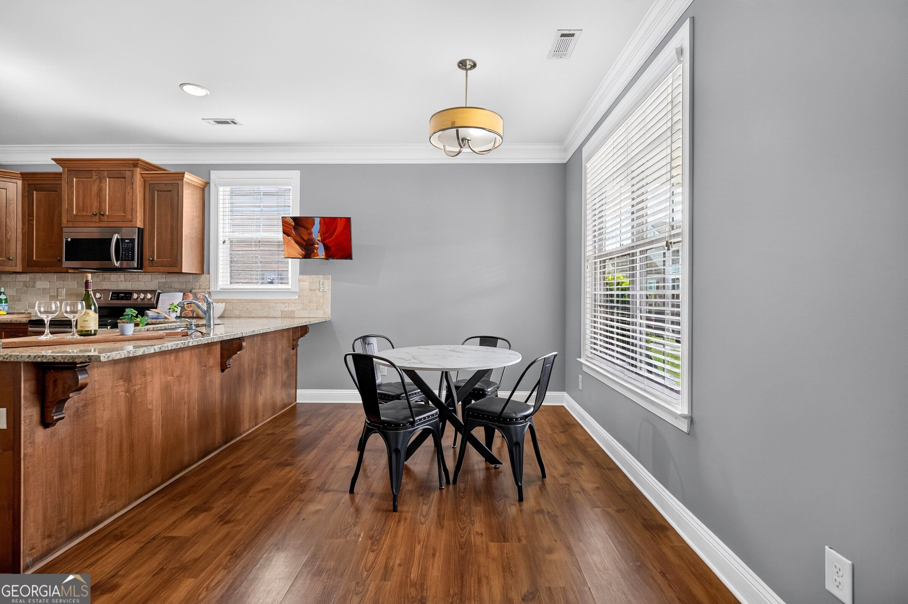 Kitchen and dining area with wood cabinetry, a granite peninsula, hardwood floors, and large windows.