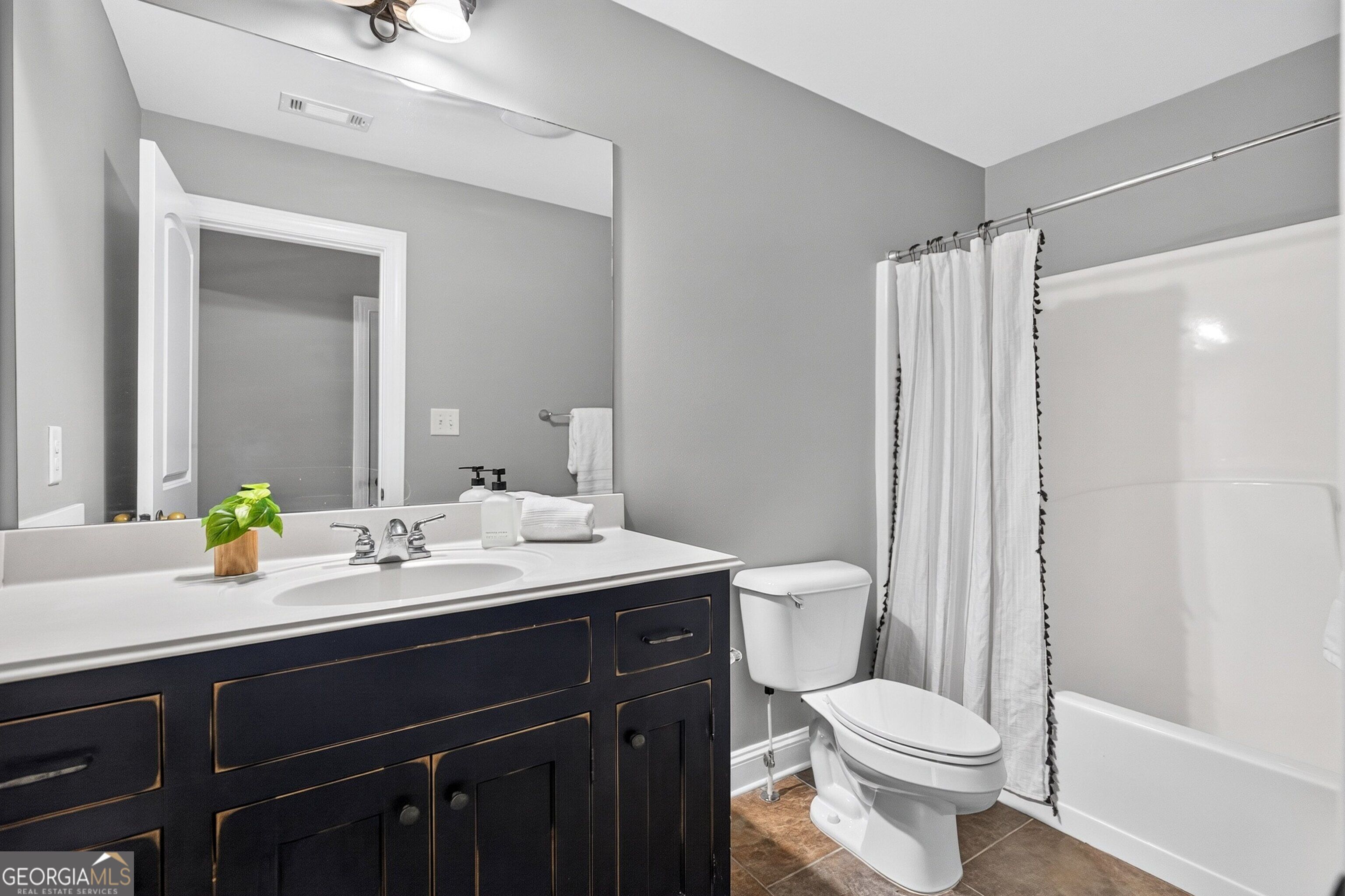 Bathroom with a navy vanity, white countertop, and tub behind a shower curtain.