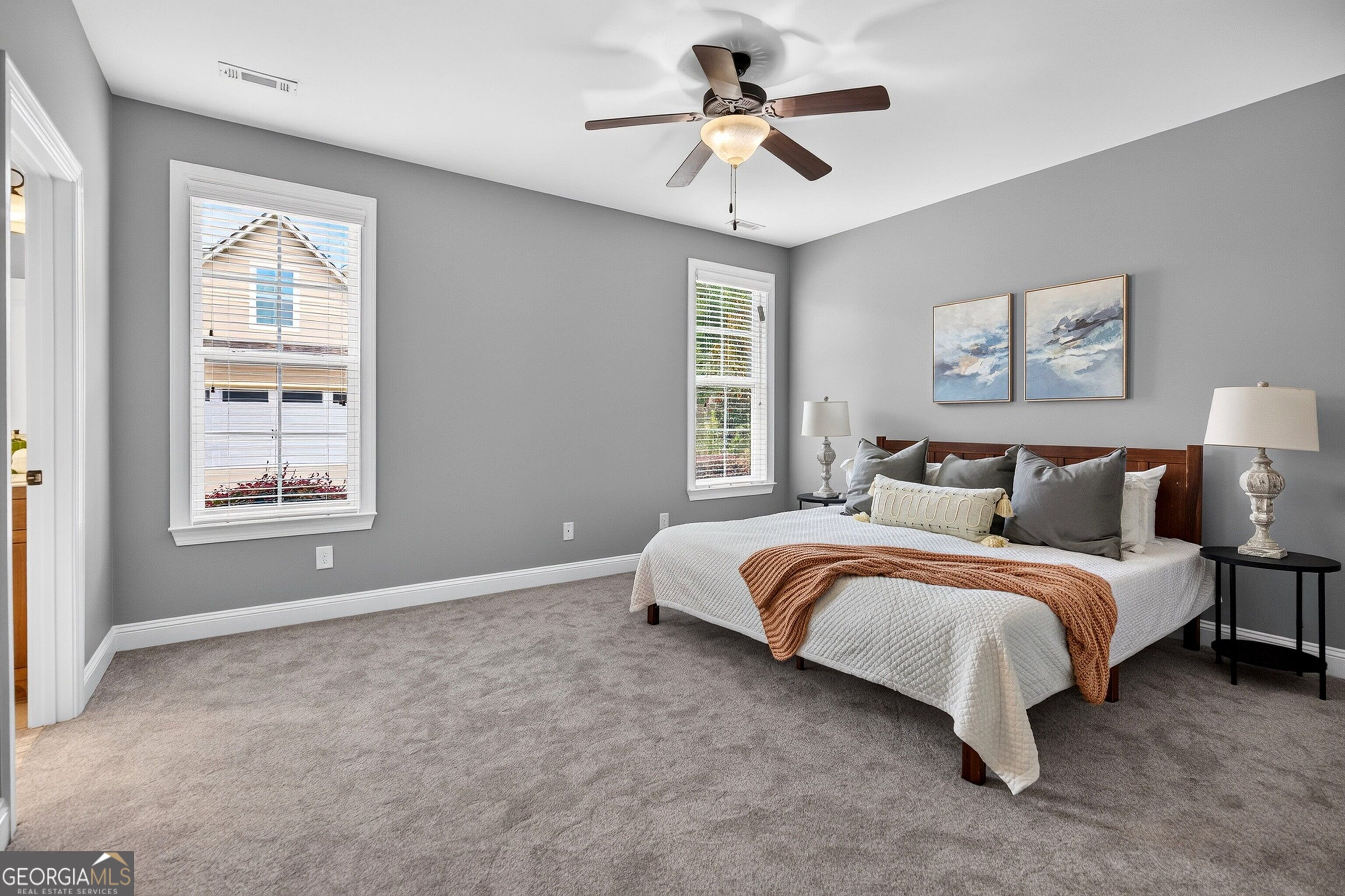 Staged bedroom with gray walls, a large bed, two windows, and a ceiling fan.