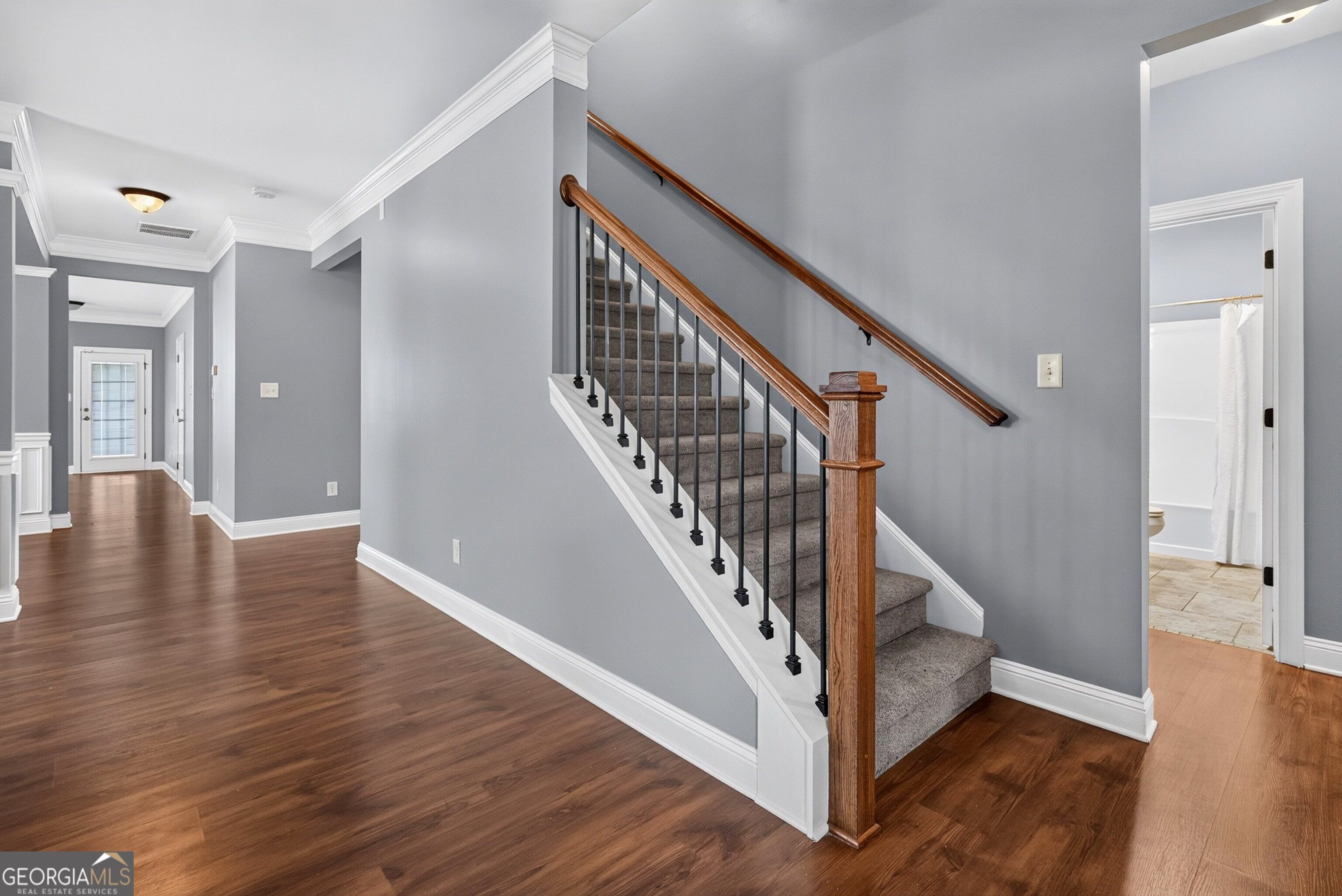 Foyer with carpeted staircase, wood handrail, black balusters, and hardwood flooring.