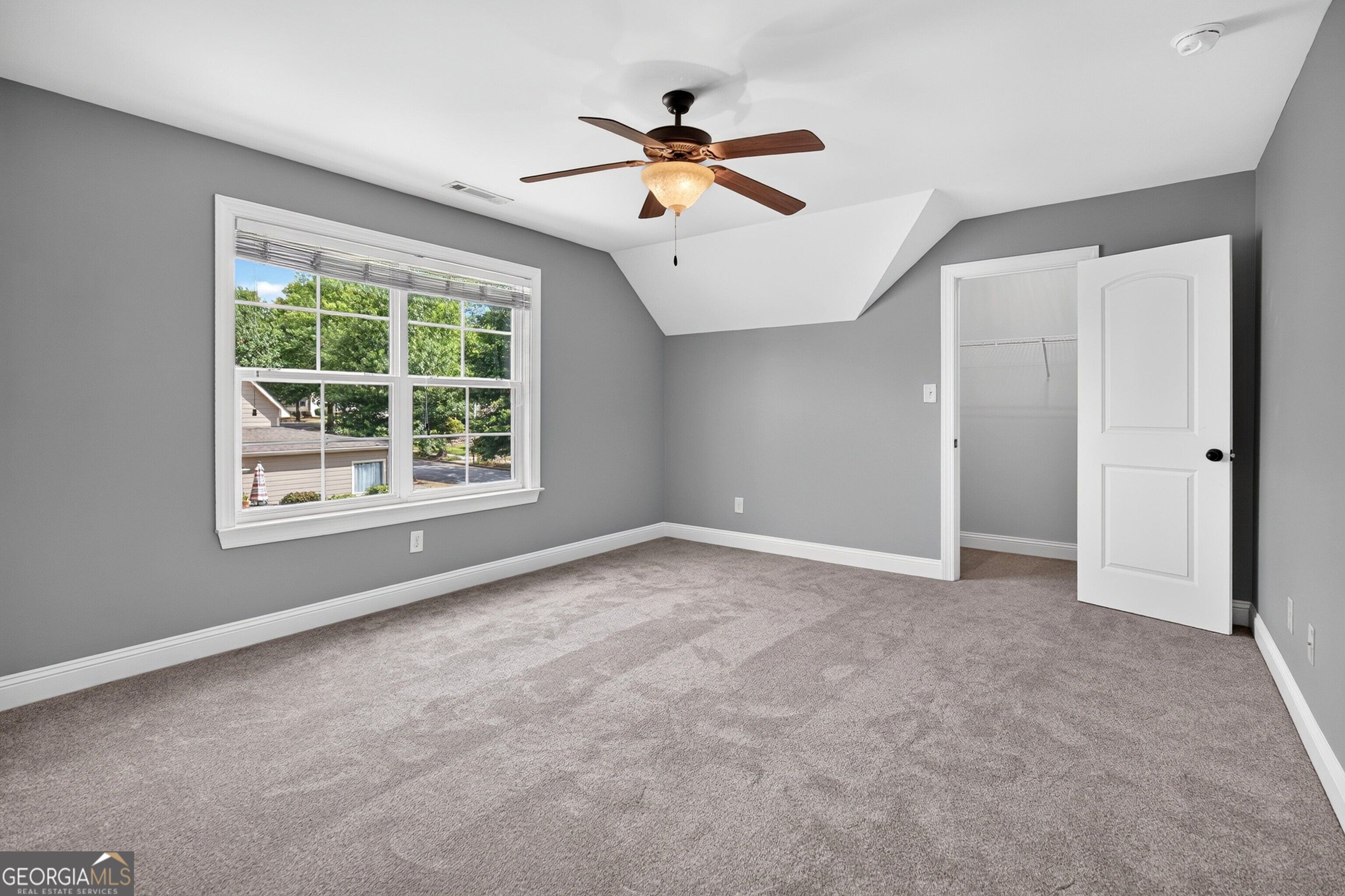 Vacant bedroom with gray walls, beige carpet, a large window, and an open closet.
