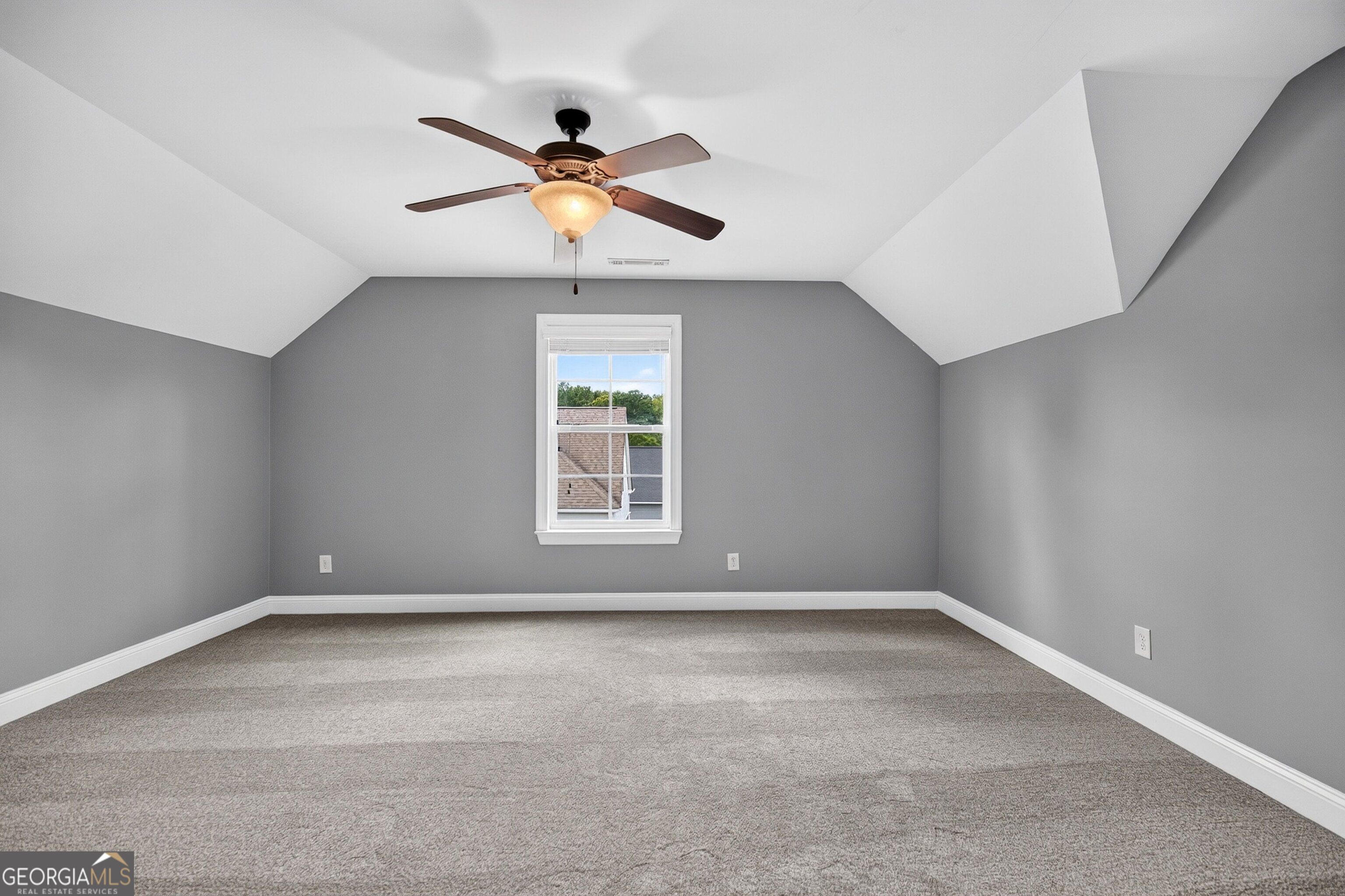 Empty carpeted room with gray walls, sloped ceiling, central window, and ceiling fan.