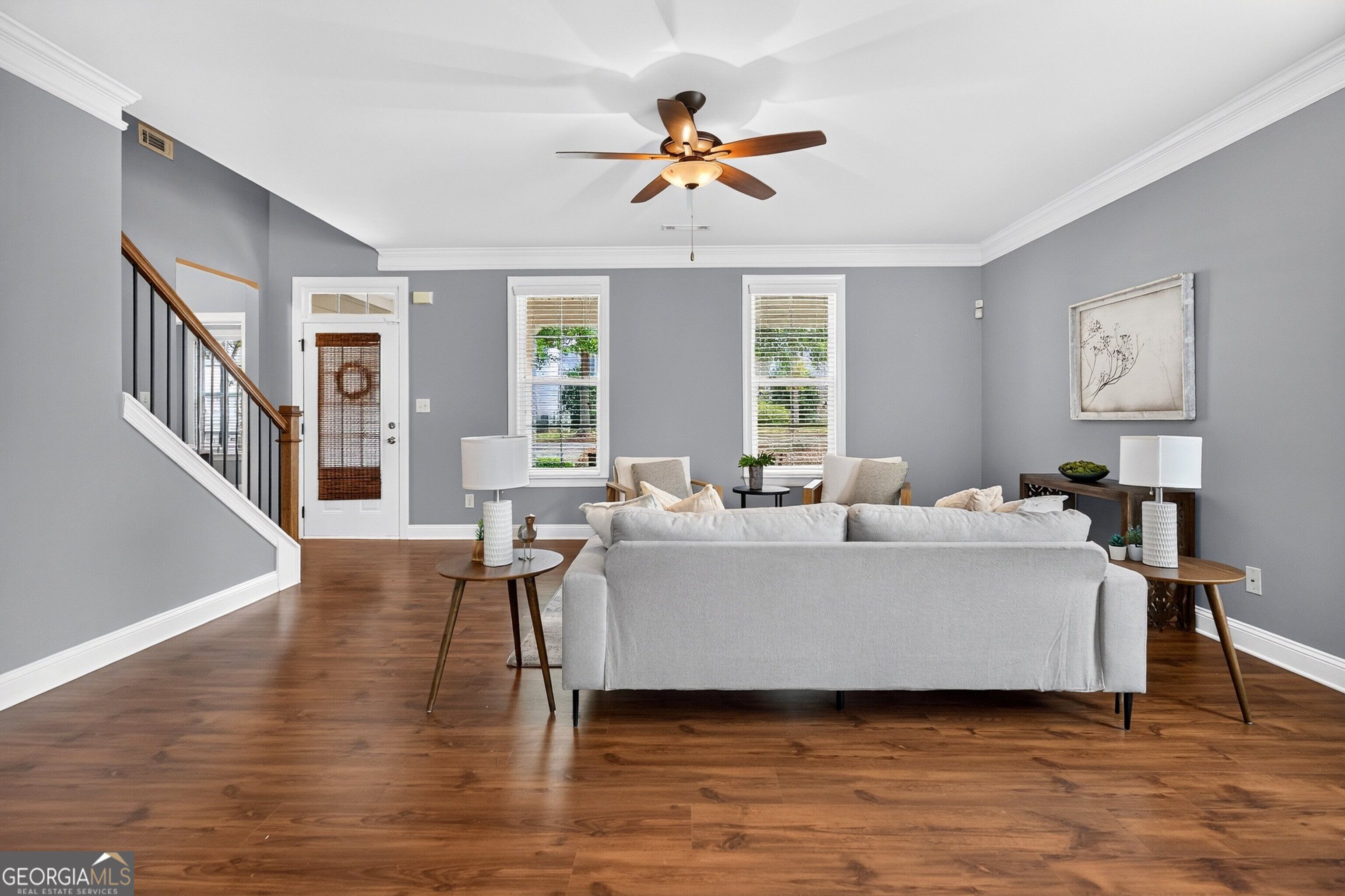 Furnished living room with a white sofa, hardwood floors, gray walls, and a staircase.