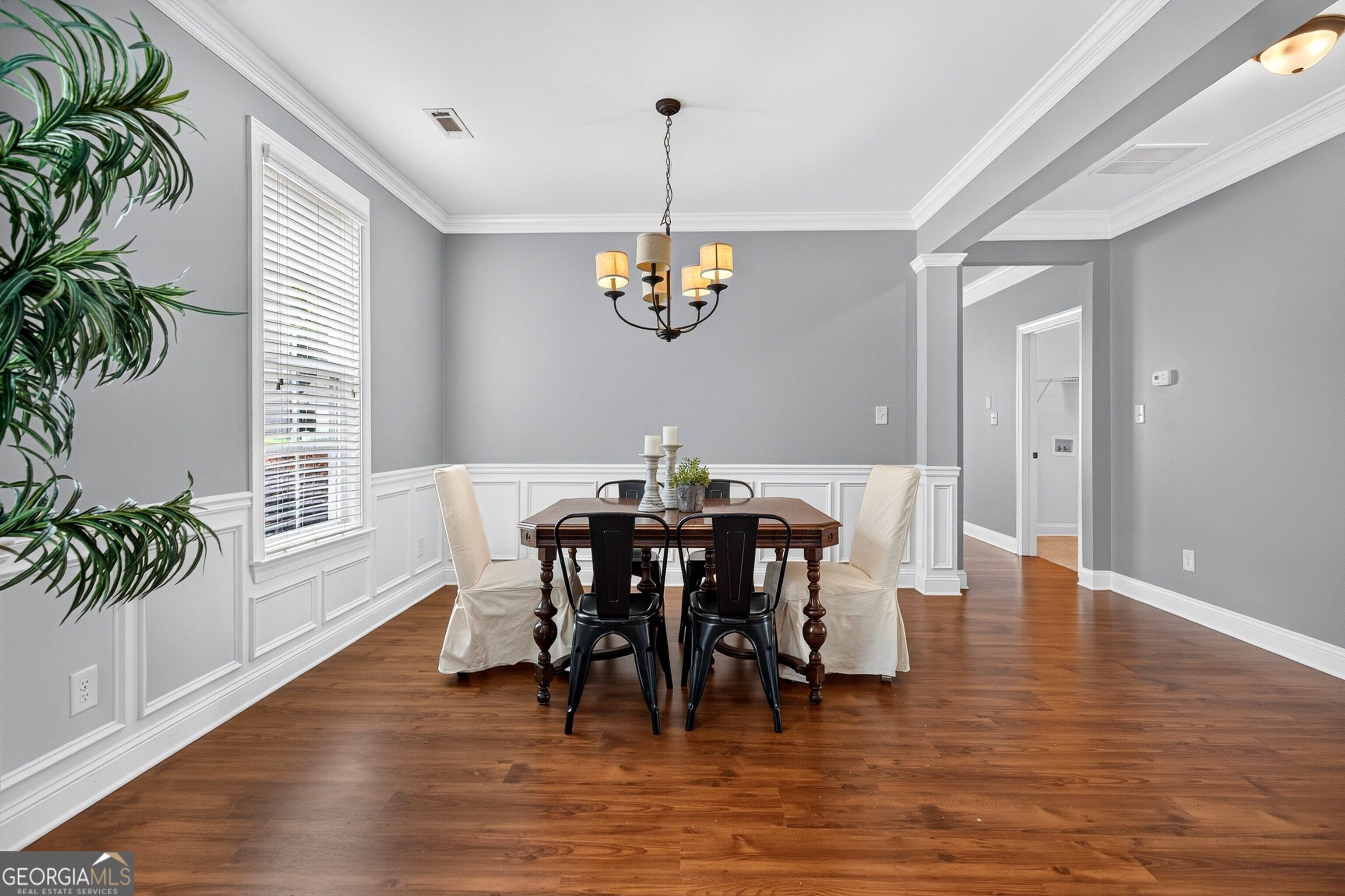 Dining room with gray walls, white wainscoting, wood flooring, and a chandelier over a furnished table.