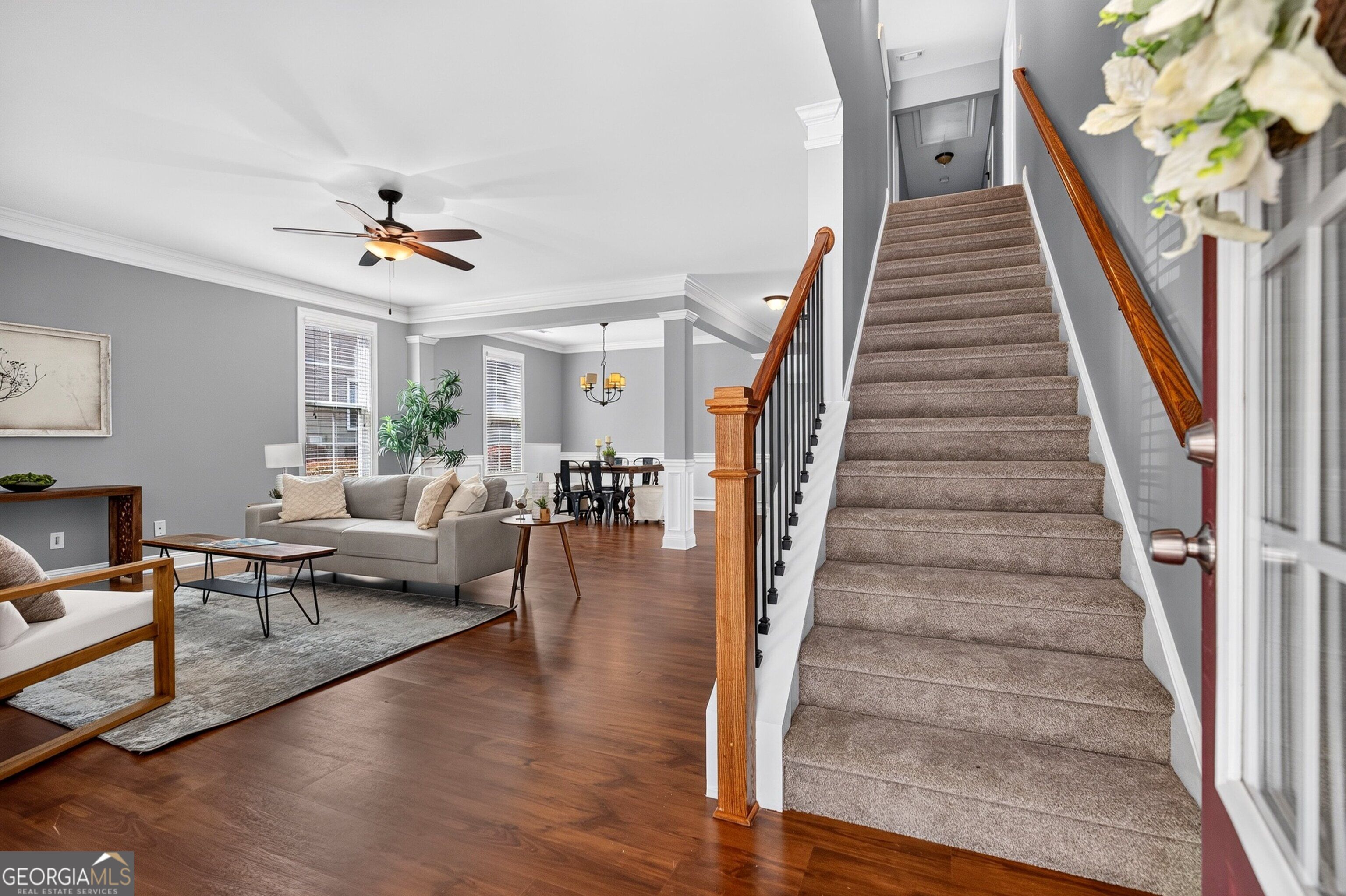 Open living and dining area beside a carpeted staircase with polished wood handrails.