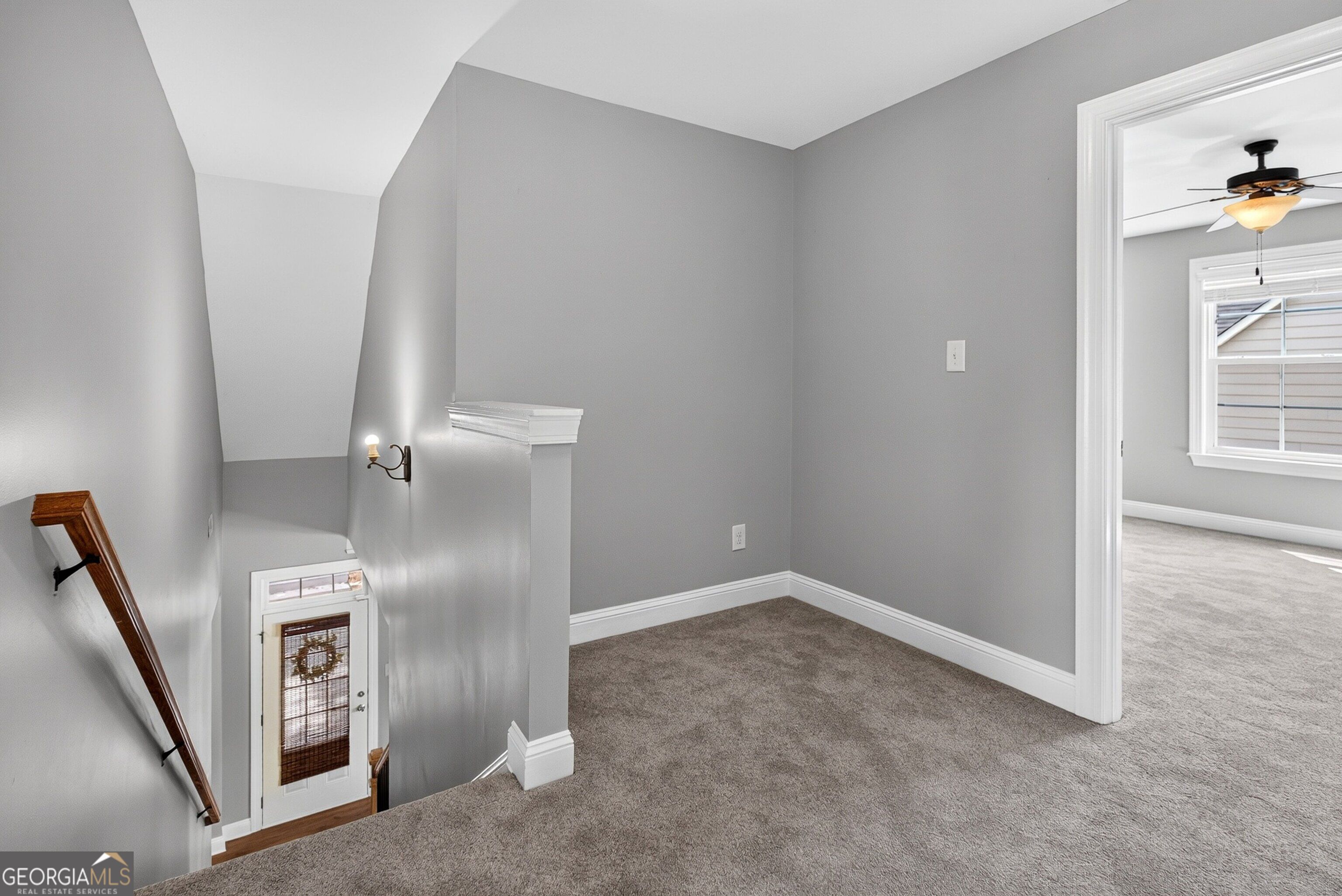 Carpeted upstairs landing overlooking a staircase, with a doorway to a room with a ceiling fan.