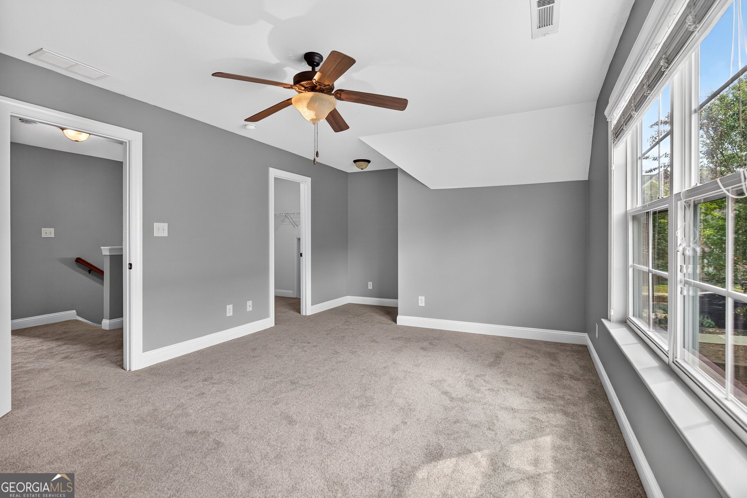 Empty carpeted room with gray walls, a ceiling fan, sloped ceiling, and large windows.