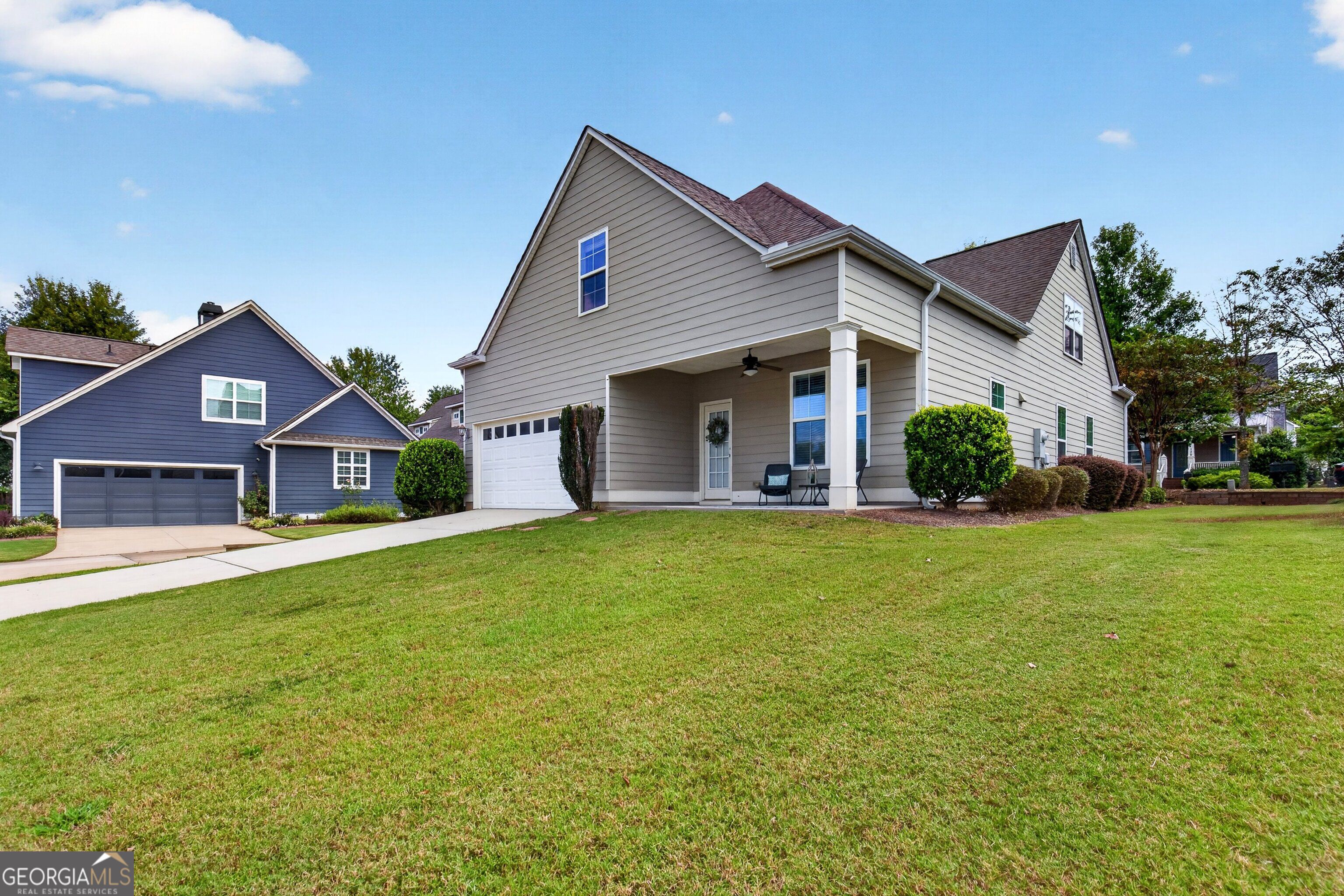 Gray two-story house with a covered porch, white garage door, and broad front lawn.