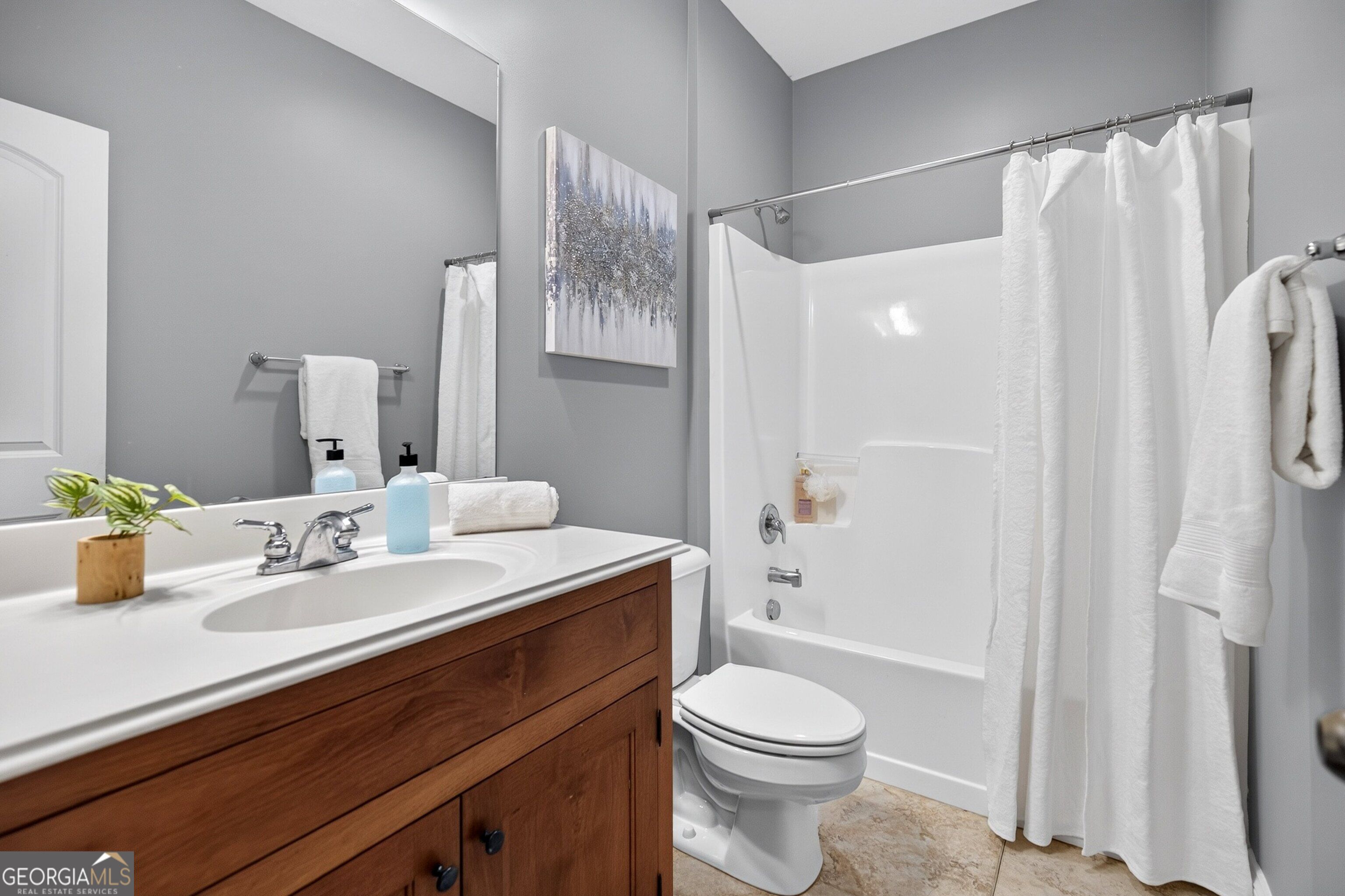 Bathroom with a wood vanity, white sink, toilet, and curtained tub-shower.