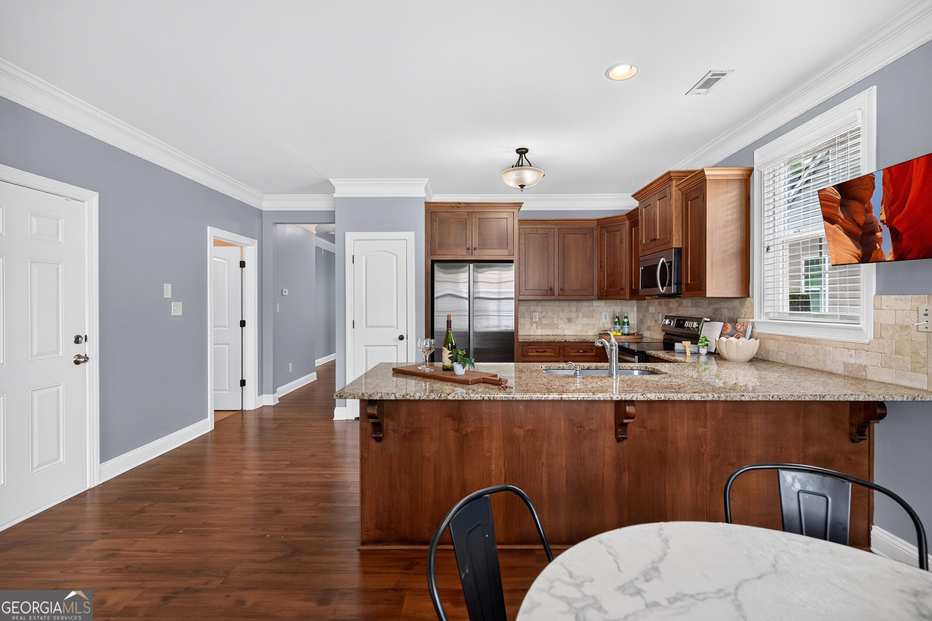 Kitchen with a granite island, dark wood cabinetry, stainless appliances, and a round dining table.