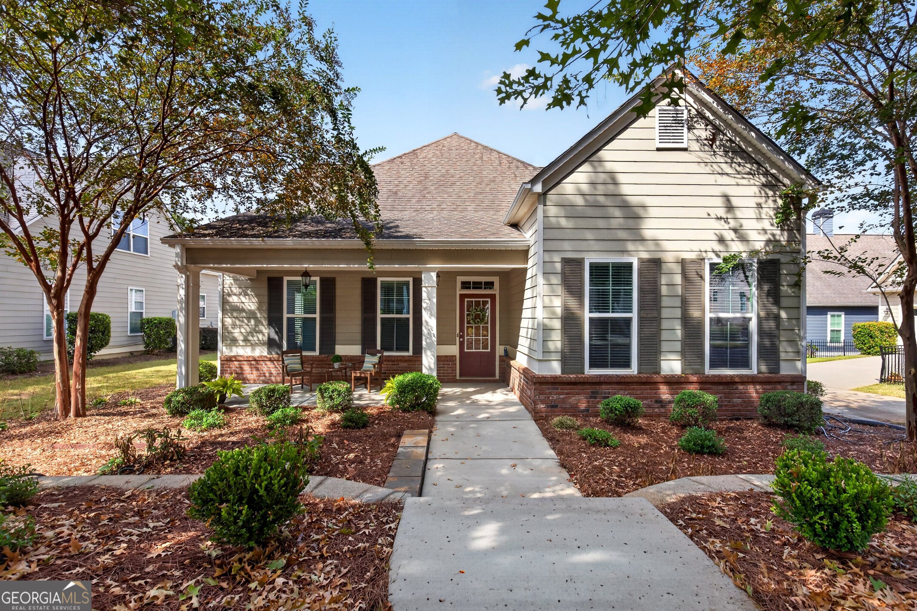 Gray-sided home with a covered porch, red front door, brick foundation, and landscaped walkway.