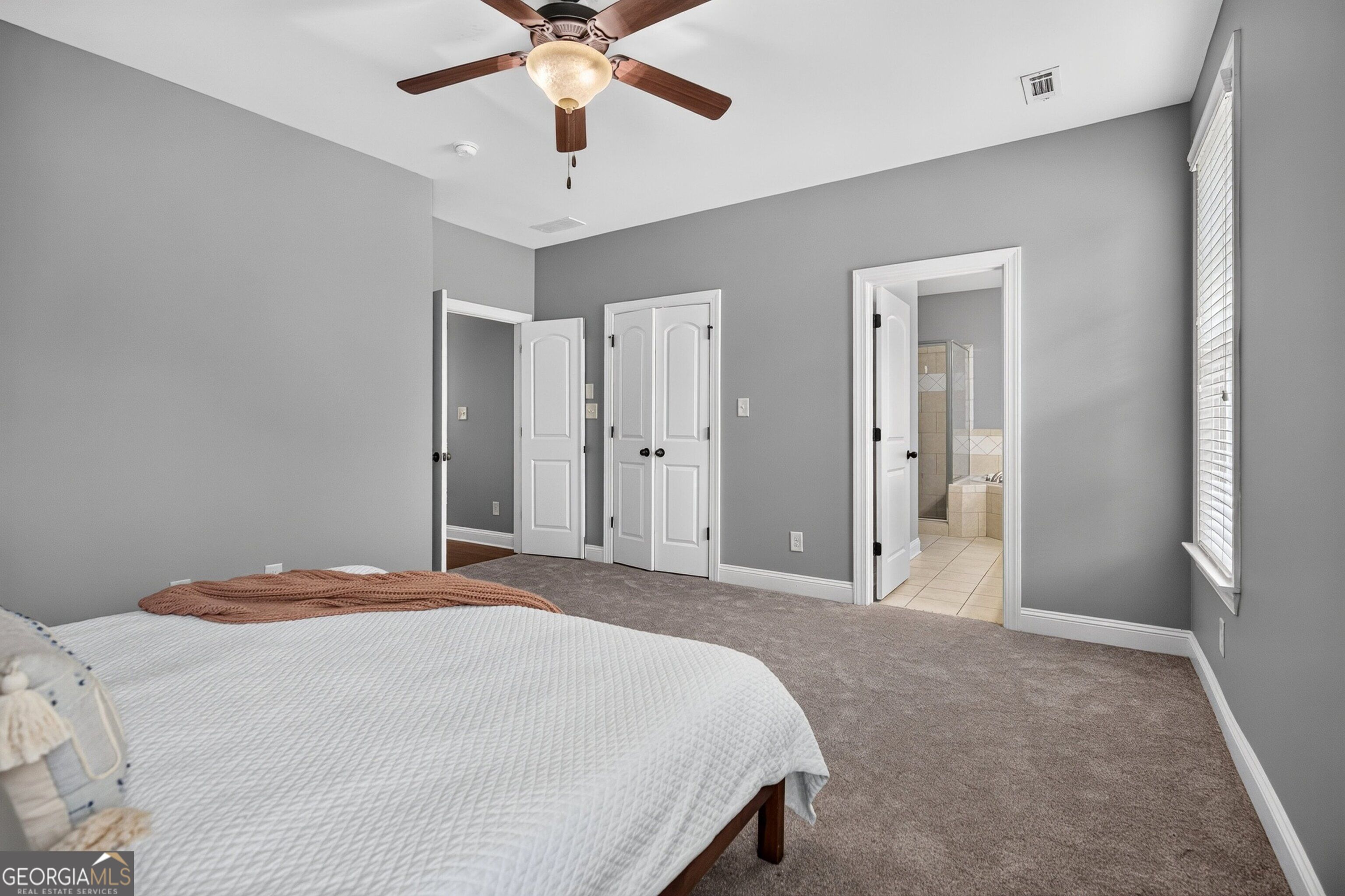 Bedroom with a white-covered bed, gray walls, and an open doorway to a tiled ensuite bathroom.