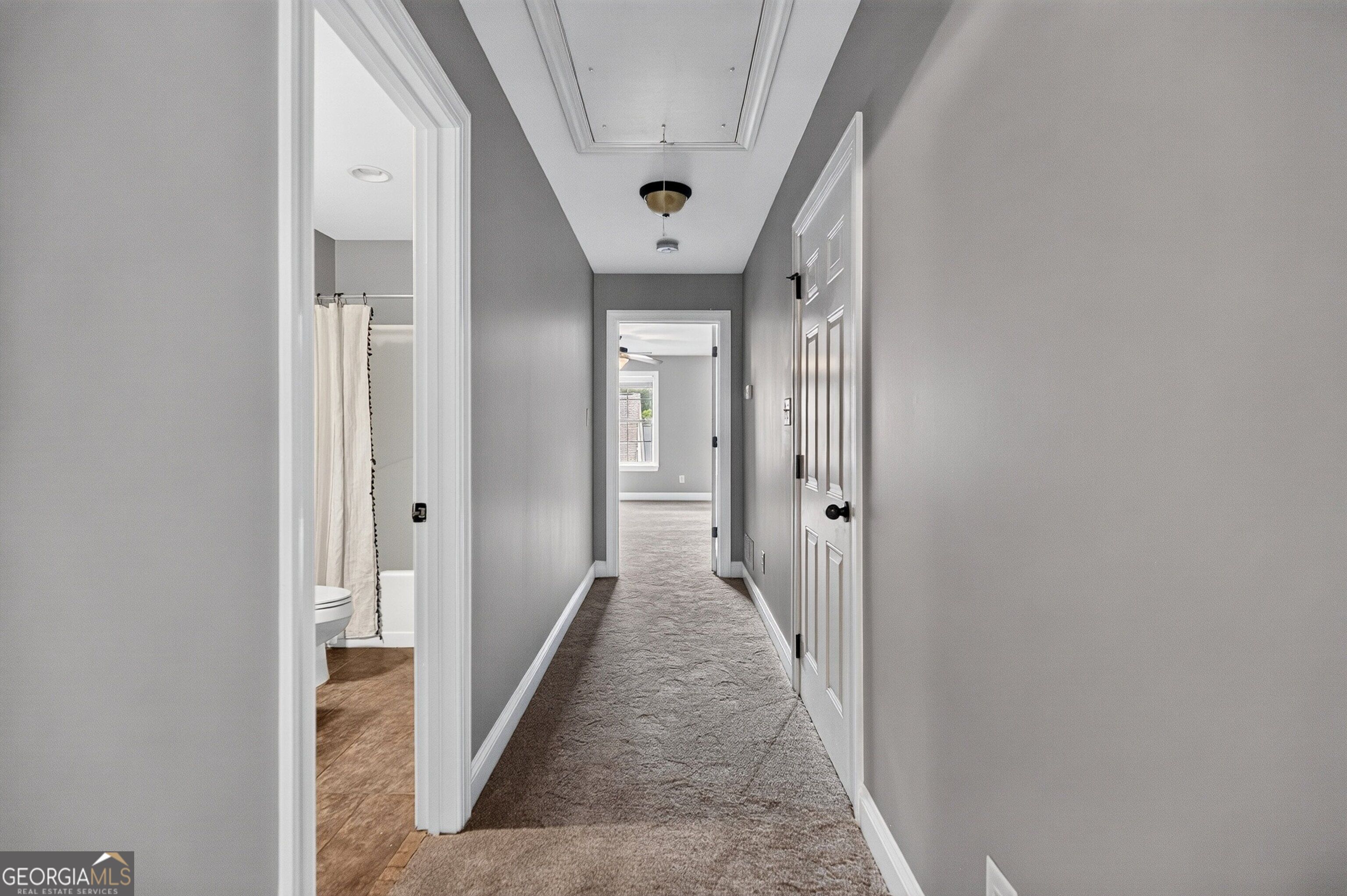 Carpeted hallway with gray walls, tray ceiling, and an open bathroom doorway.