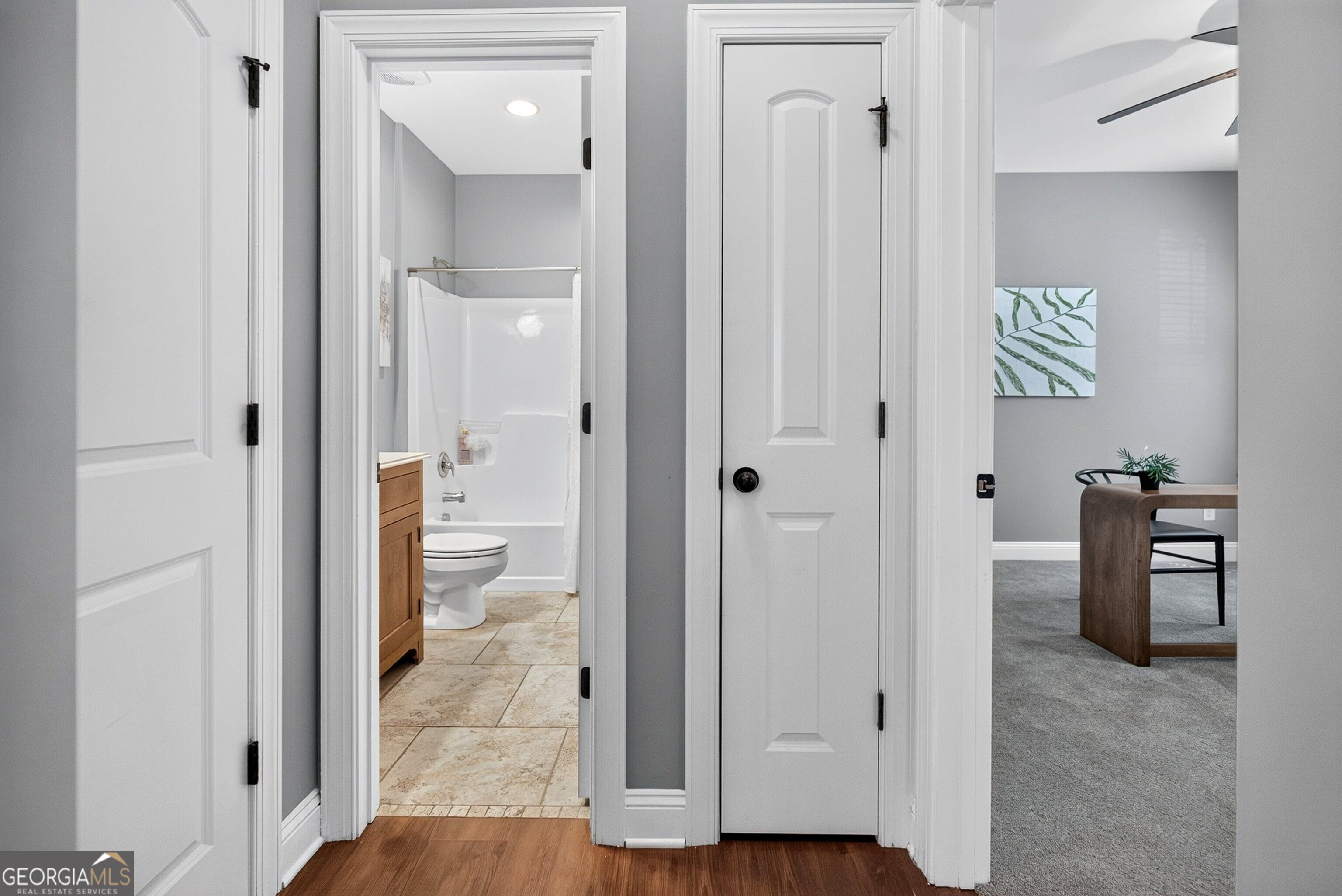 Hallway opens to a tiled bathroom and a carpeted room with a desk and chair.