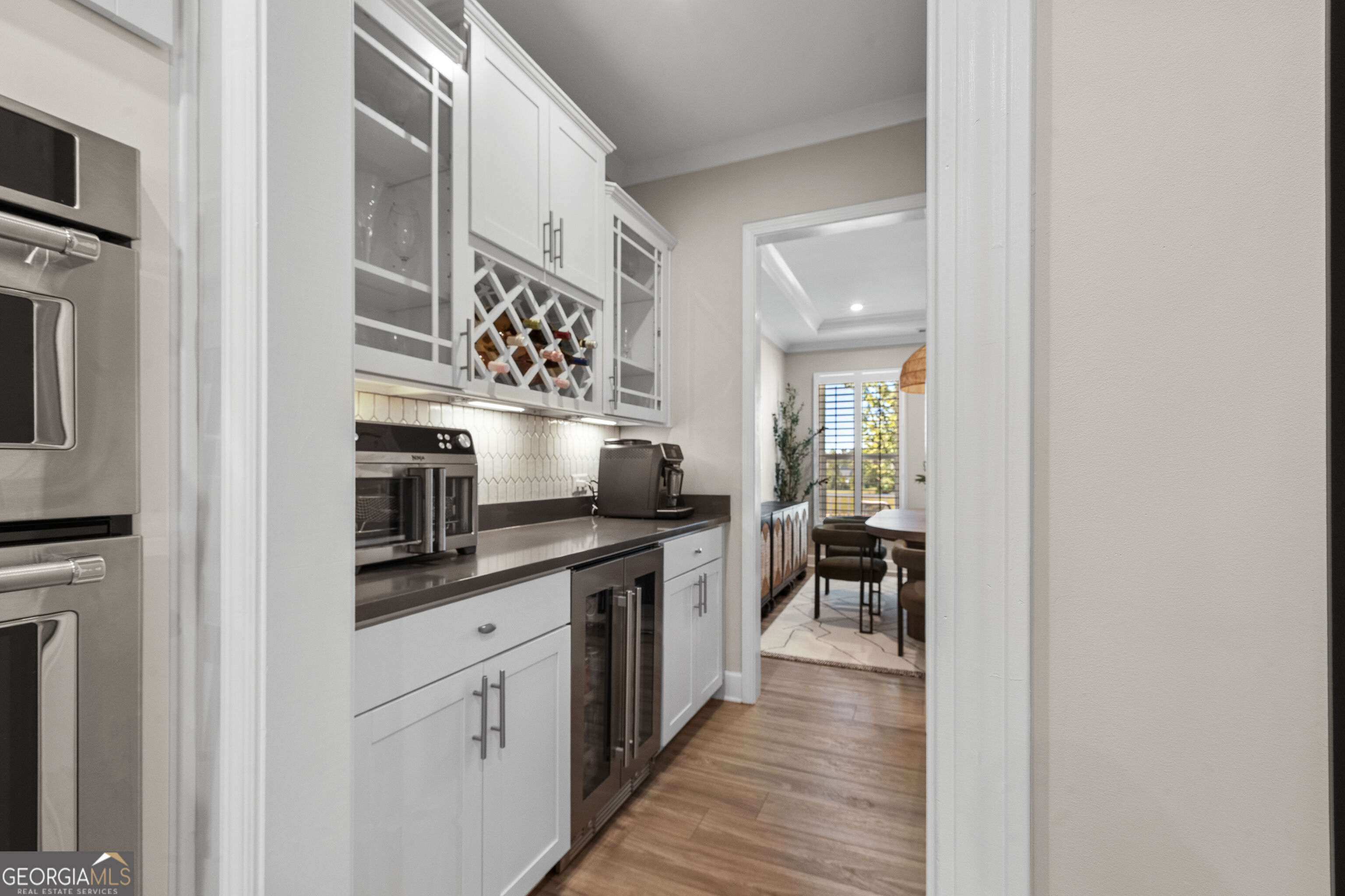 Kitchen beverage station with a built-in wine rack and glass-front cabinets, opening onto a dining area.