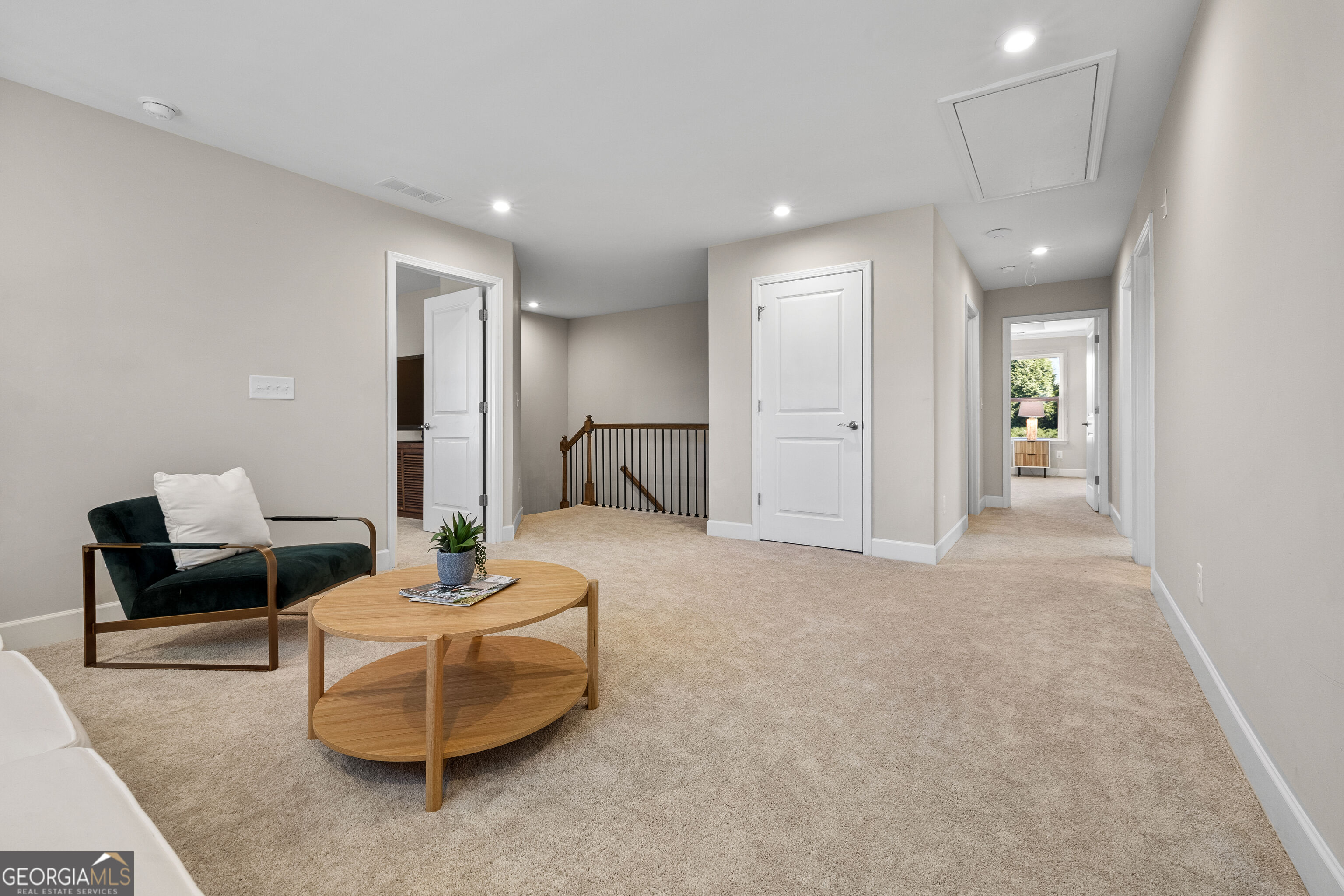 Upstairs sitting area with a dark green armchair, round wood table, and hallway overlooking the stairwell.