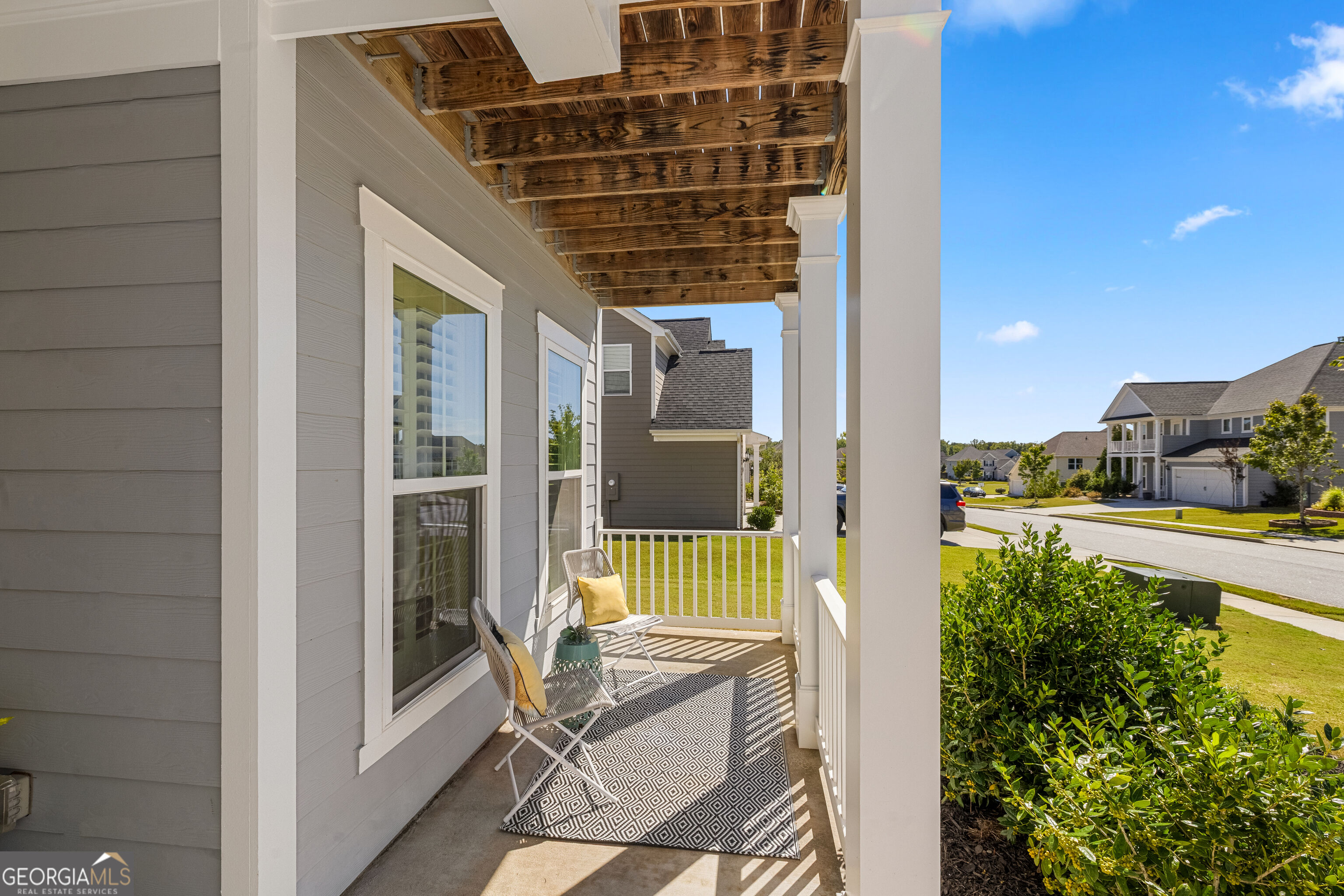 Covered front porch with exposed wood beams, white columns, seating, and a view of the neighborhood.