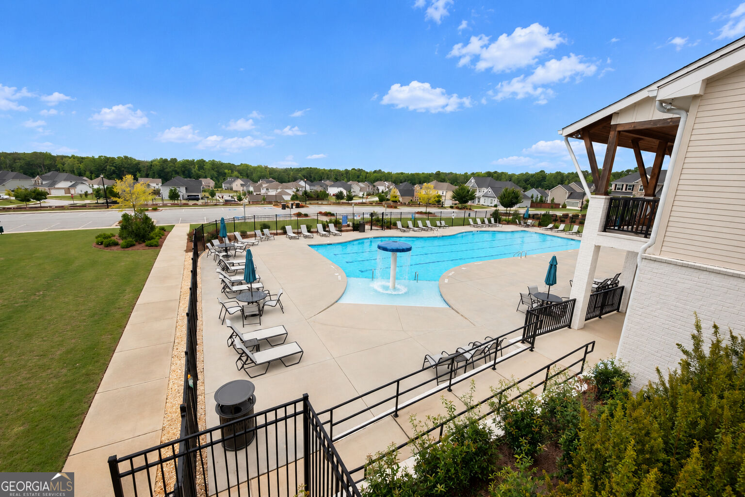 Community pool with a shallow splash area, central water feature, lounge chairs, and clubhouse.