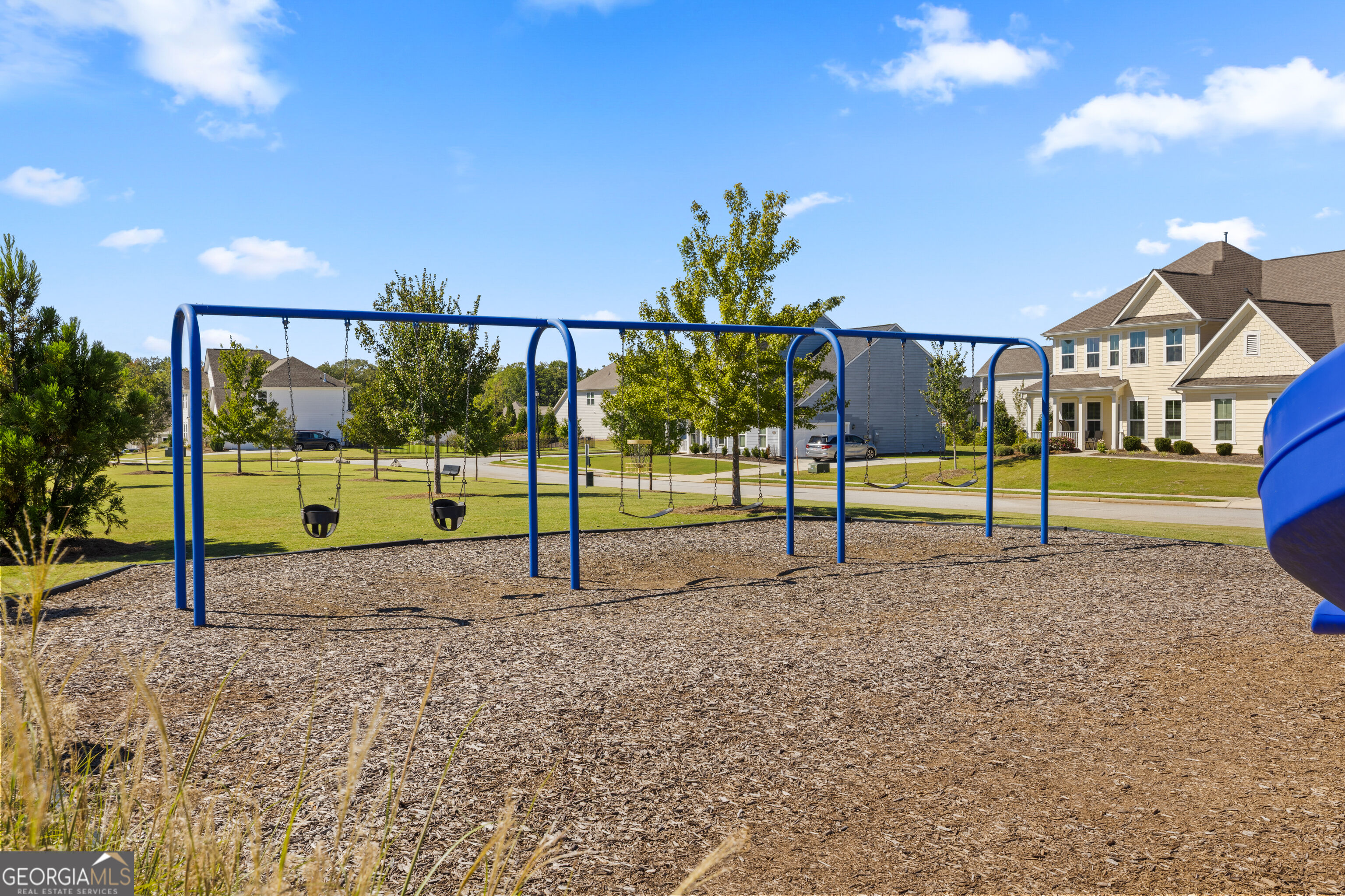 Neighborhood playground with blue swings and a slide, surrounded by homes and lawns.