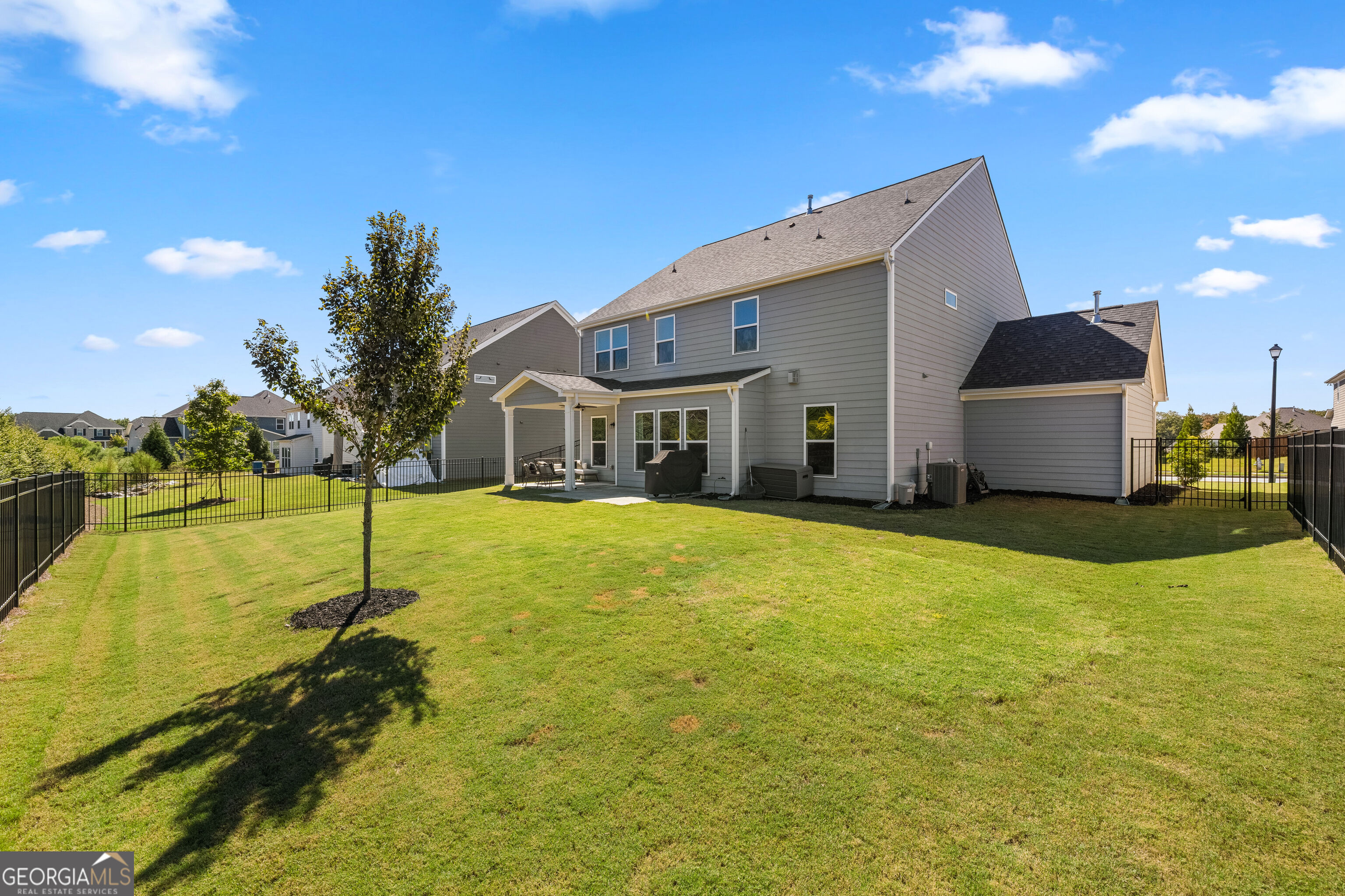 Rear of a gray two-story home with a covered patio, attached garage, and fenced lawn.