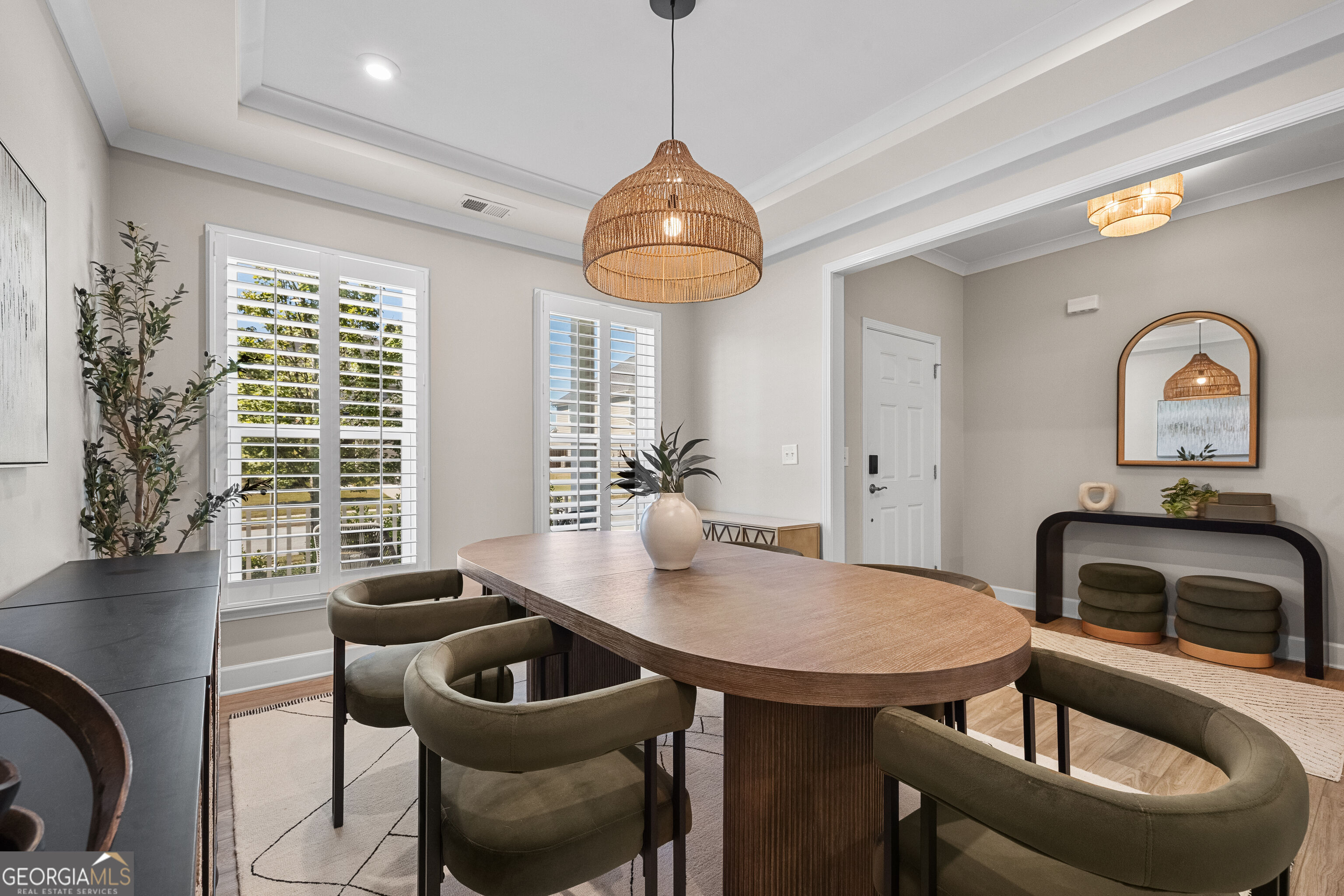 Dining room with an oval wood table, olive chairs, plantation shutters, and a woven pendant light.