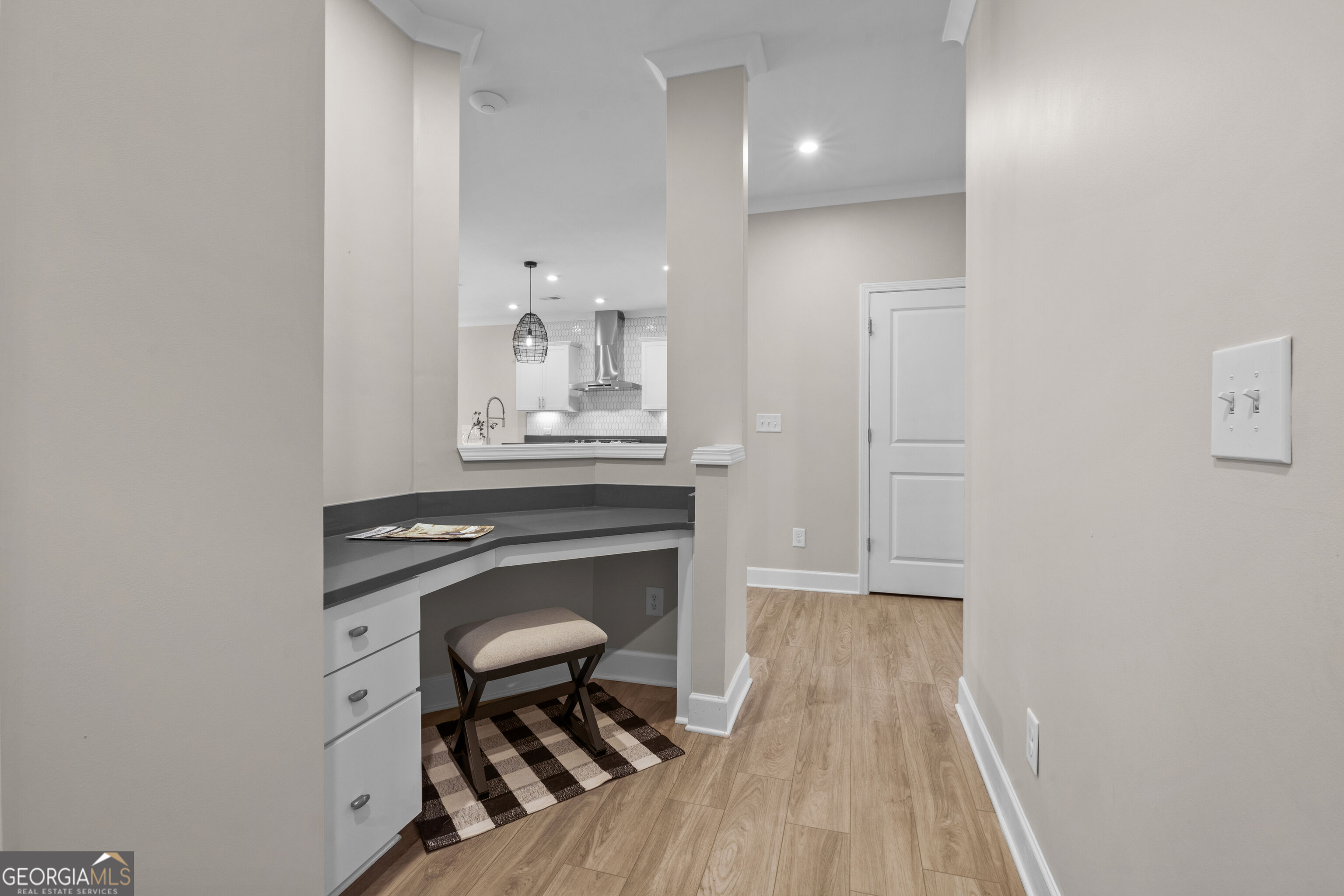 Hallway with a built-in desk nook, cushioned stool, and the kitchen visible beyond.