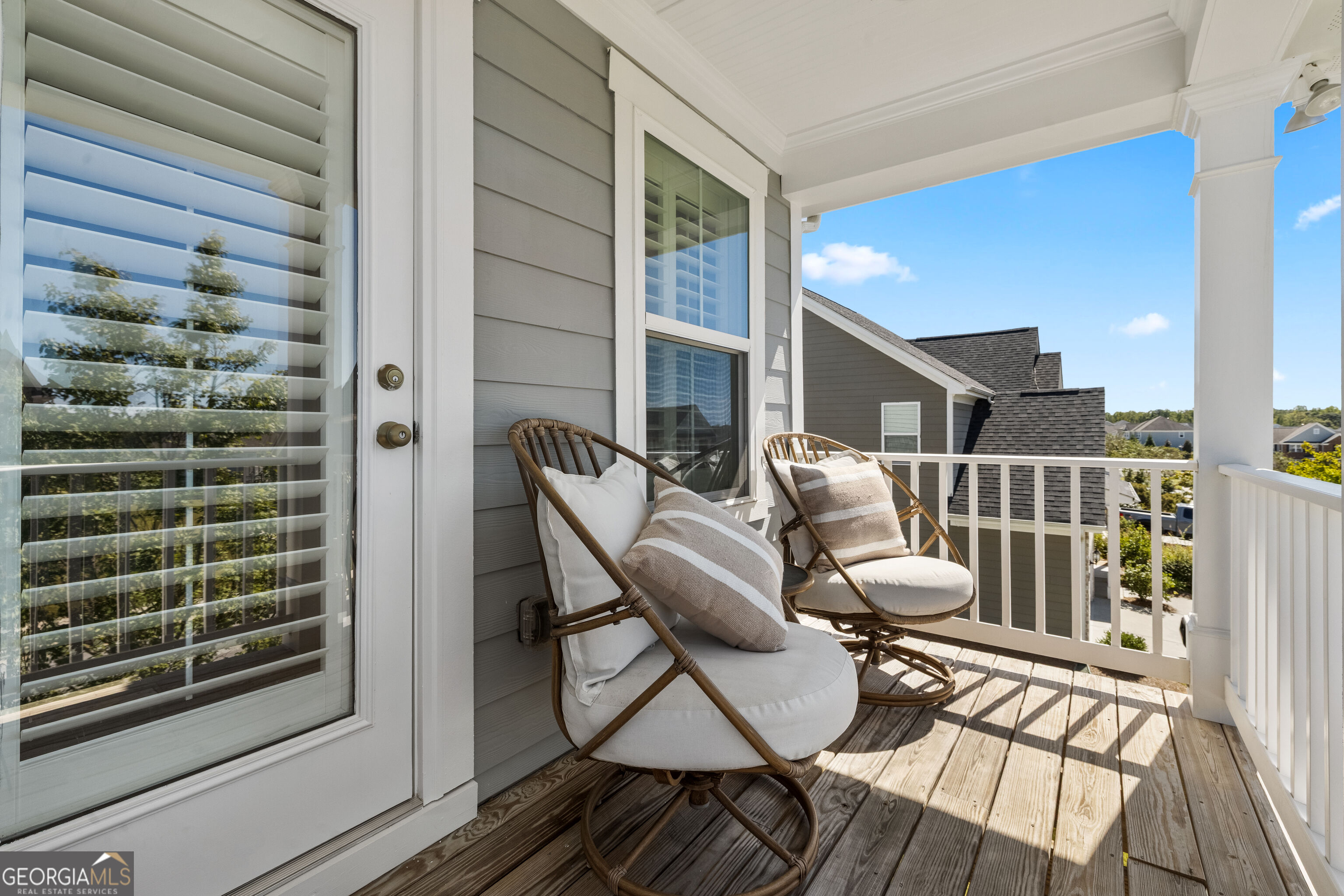 Covered balcony with two cushioned wooden chairs and views of neighboring homes.