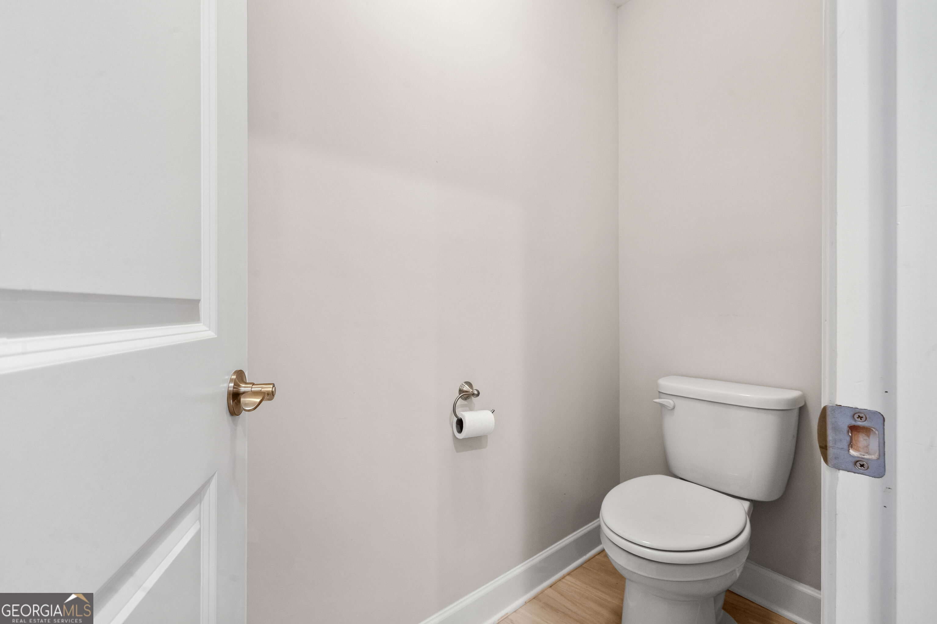 Small bathroom with a white toilet, neutral walls, and light wood flooring.