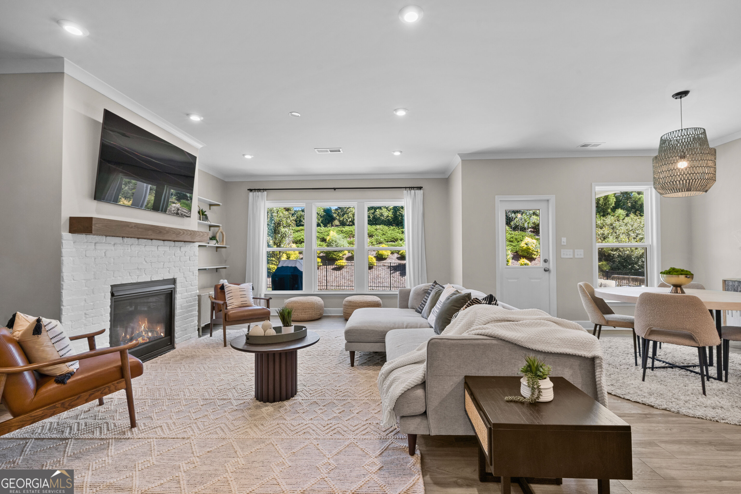 Living room with a white brick fireplace, gray sectional, and large garden-facing windows.