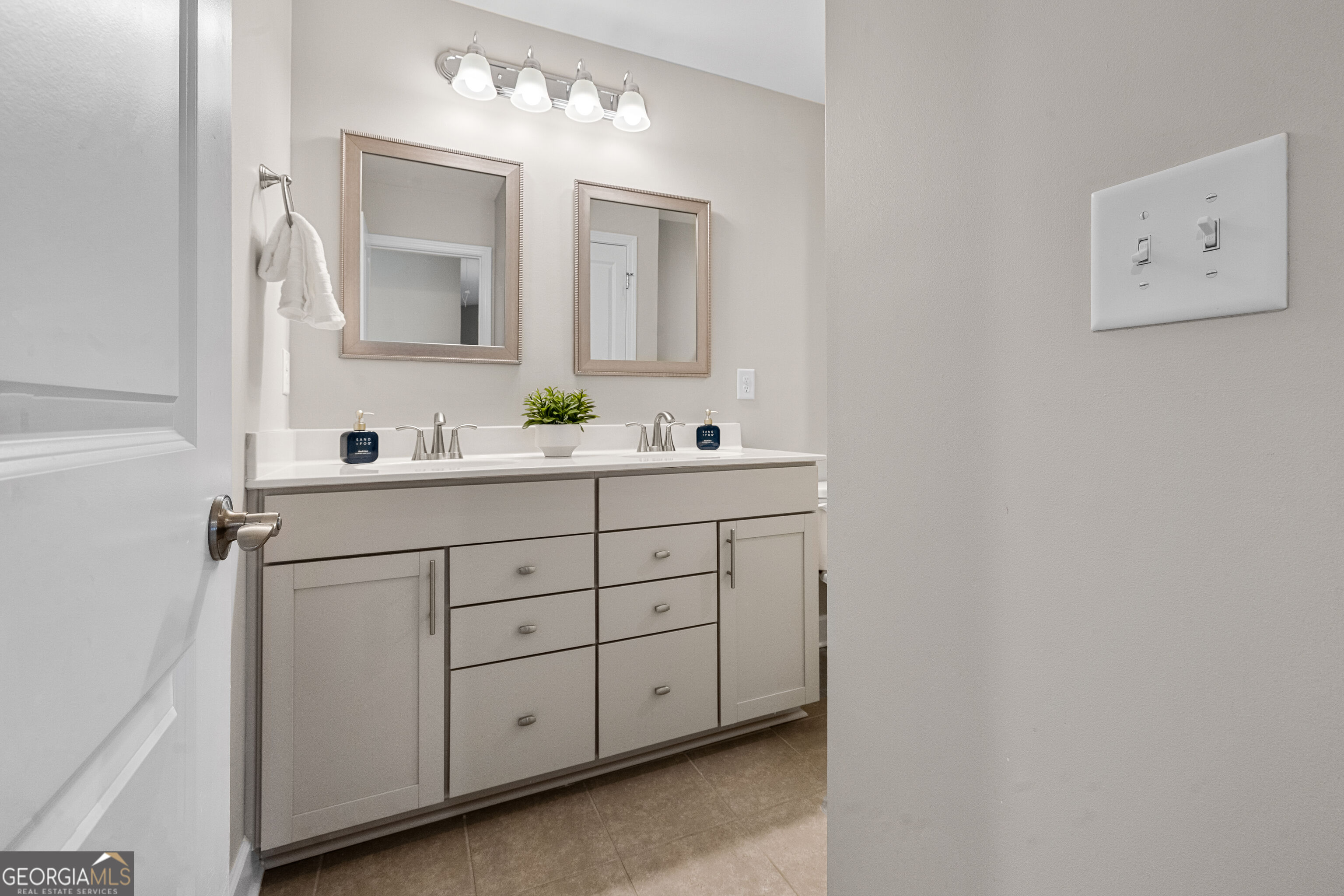 Bathroom with a double-sink vanity, gray cabinetry, and two framed mirrors.