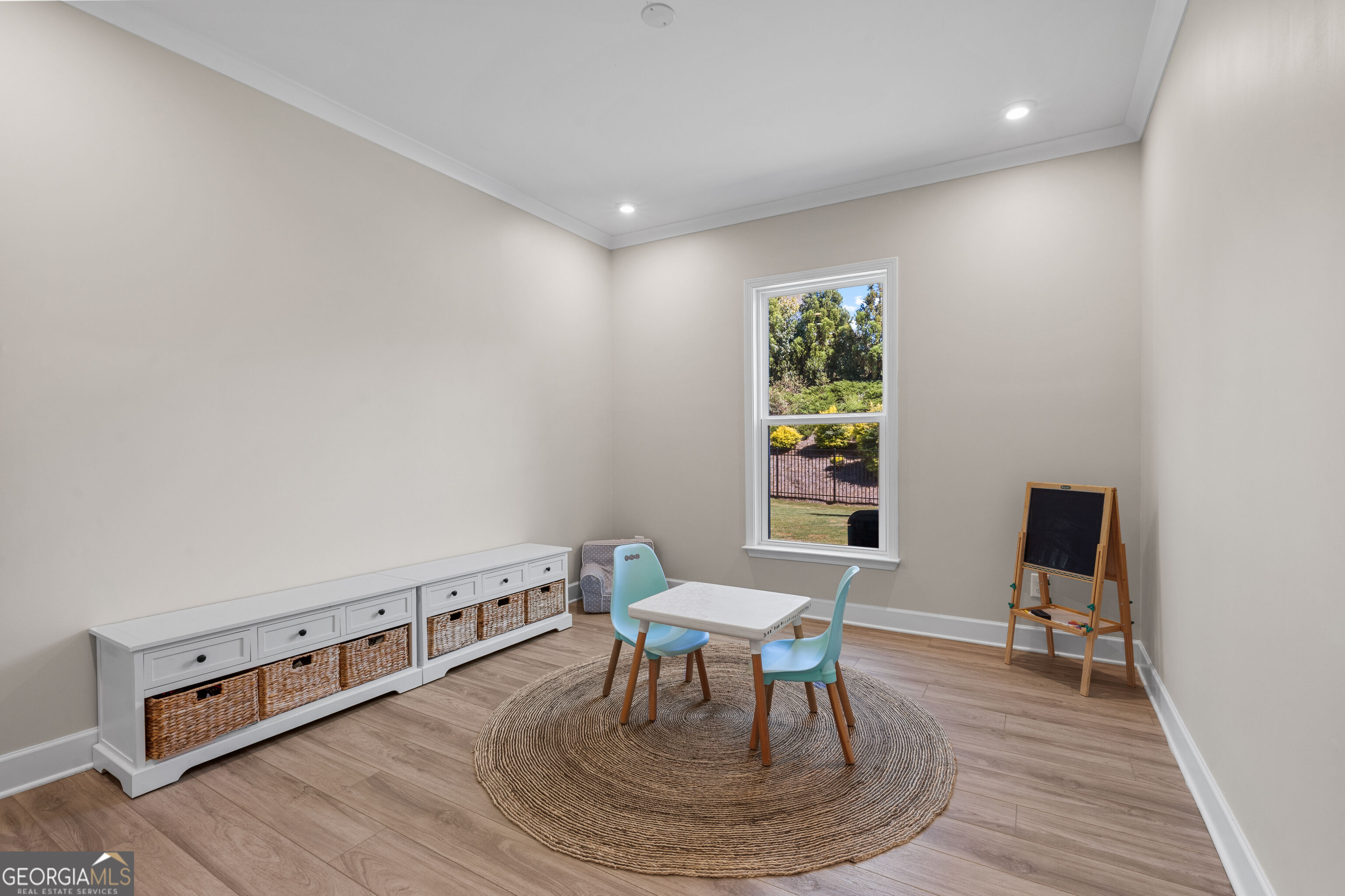Furnished playroom with a child-sized table, blue chairs, woven rug, and chalkboard easel.
