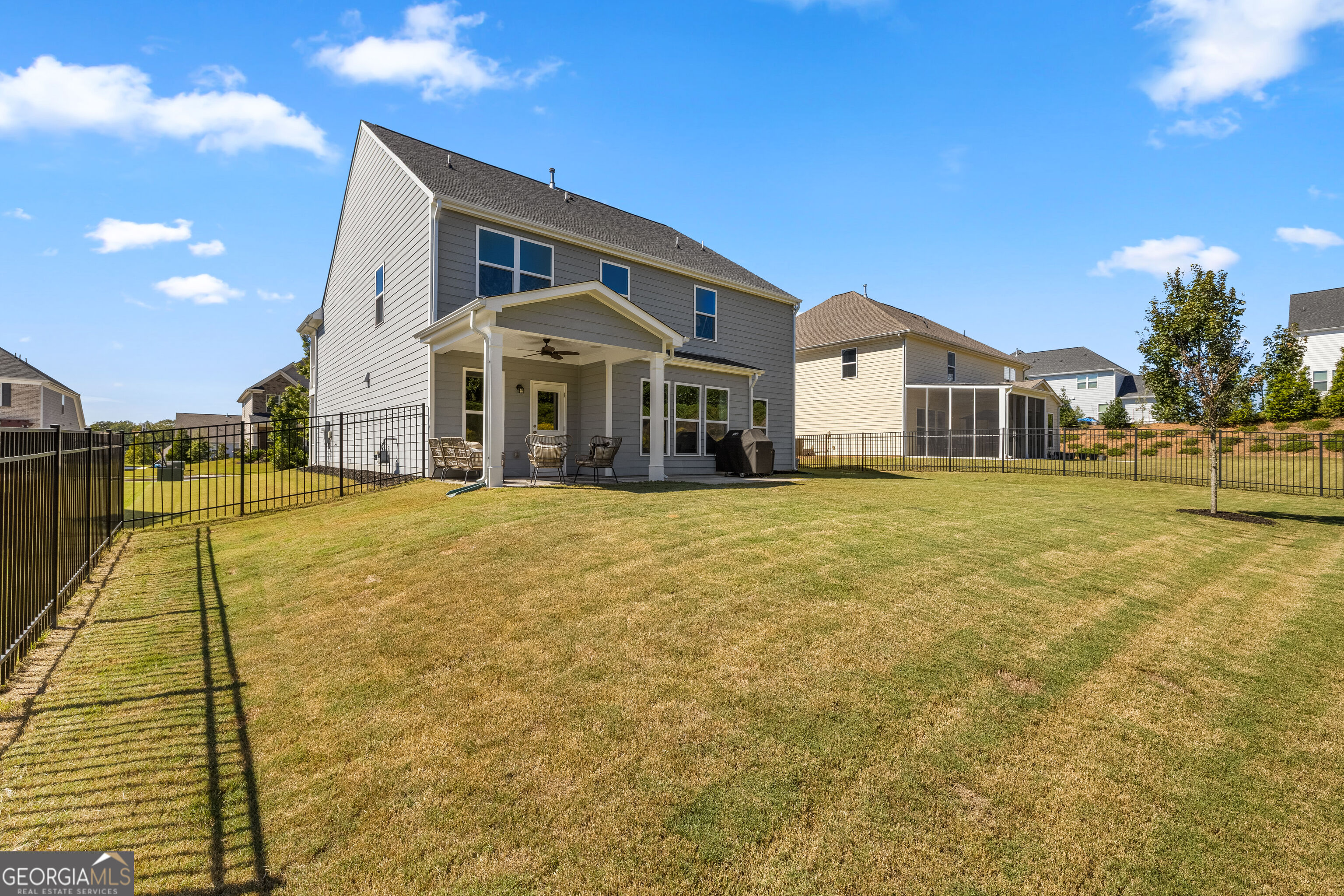 Gray two-story home with covered patio and seating overlooking a fenced backyard.