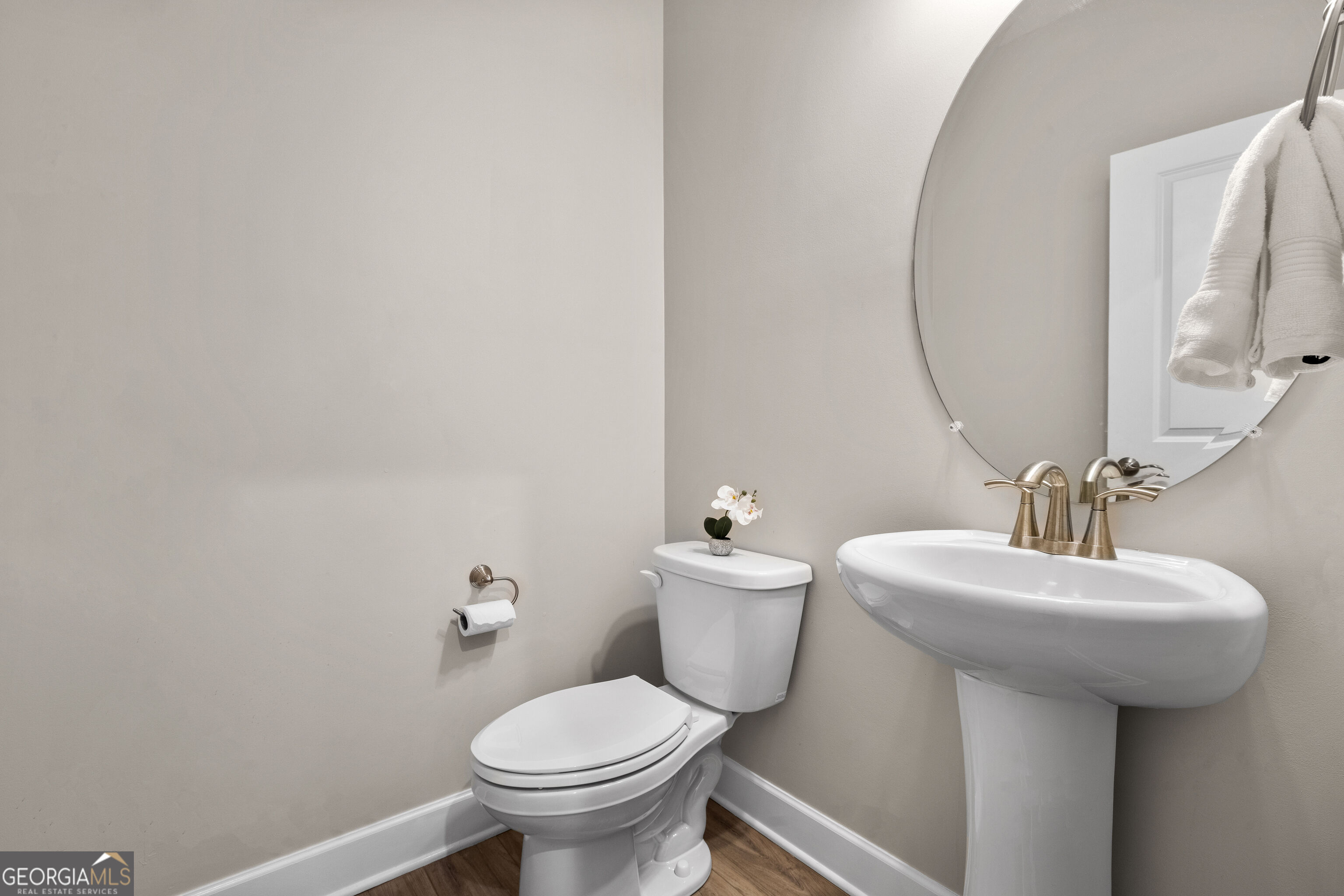 Bathroom with a white pedestal sink, toilet, round mirror, and bronze-tone fixtures.