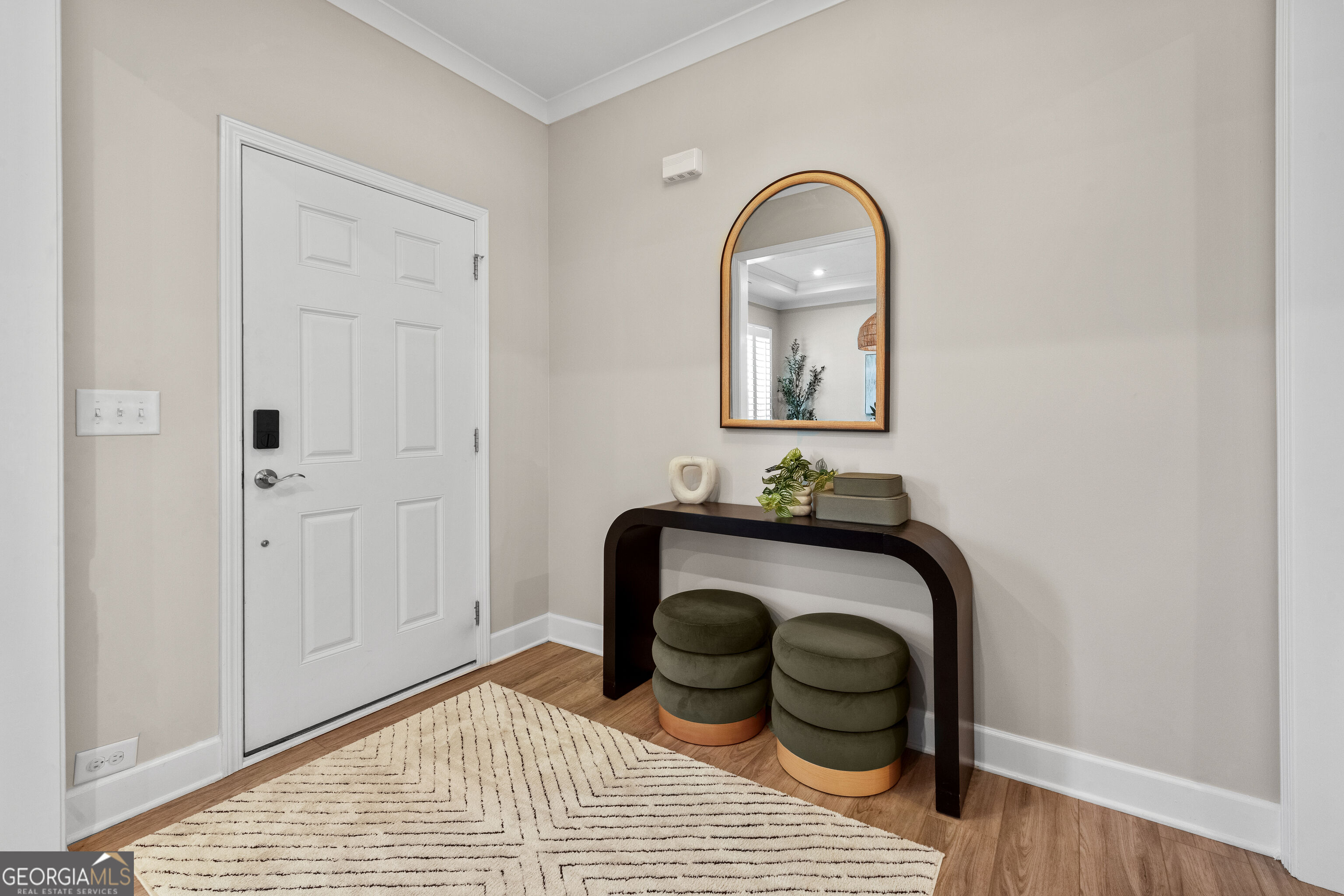 Staged entryway with a white front door, arched mirror, dark console table, and round stools.
