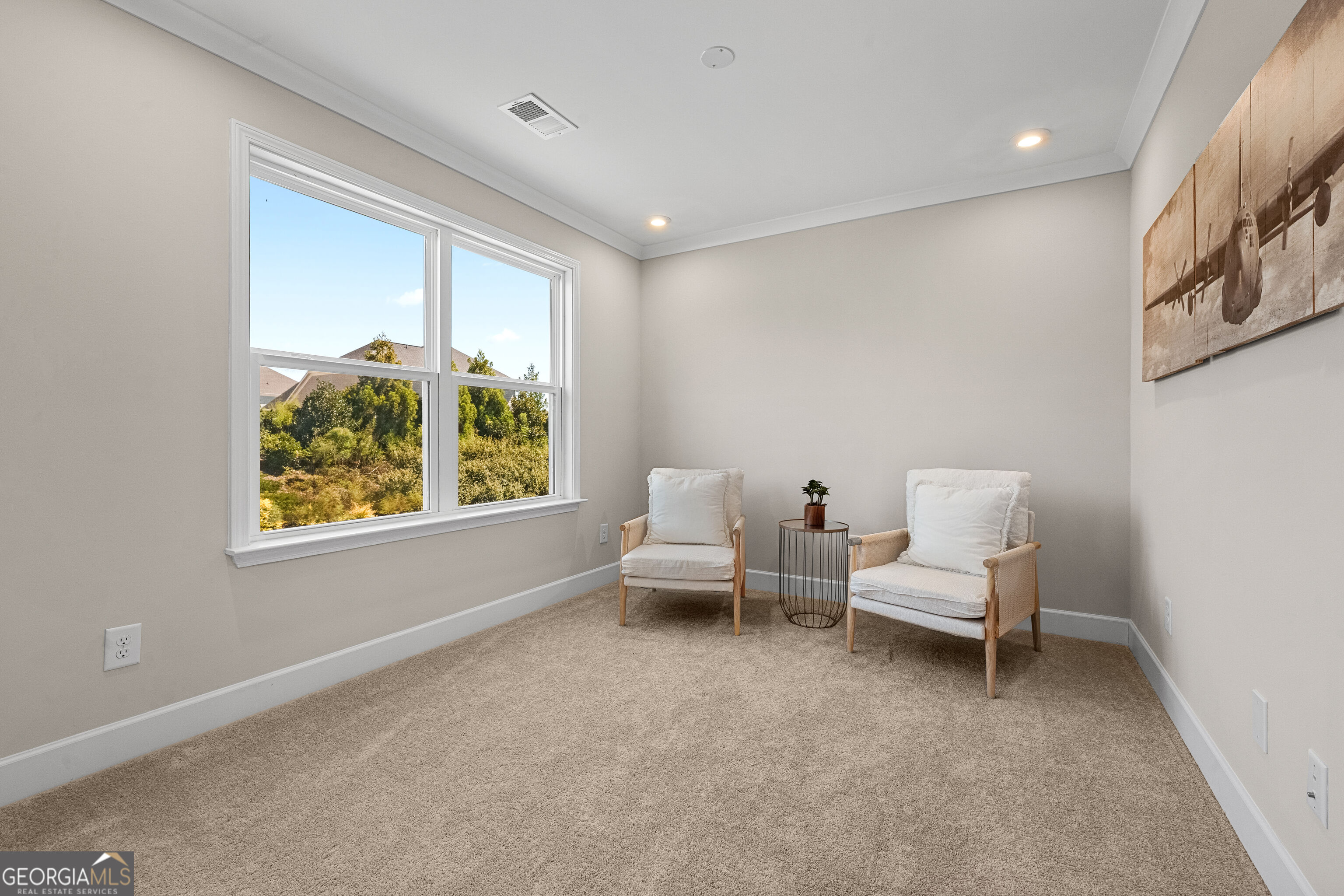 Sitting area with two light chairs beside a large window overlooking greenery.