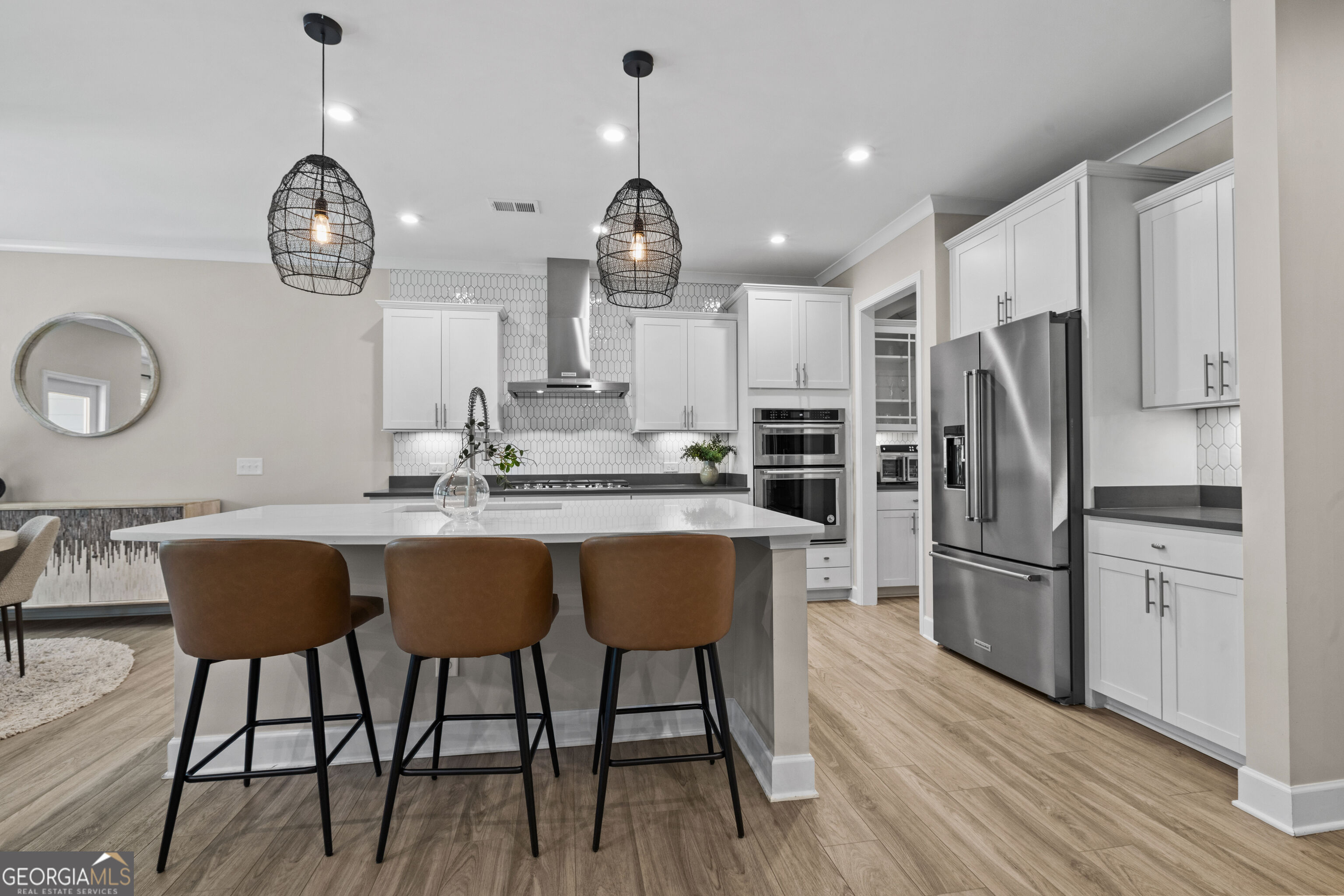 Modern kitchen with a large white island, brown bar stools, and stainless steel appliances.