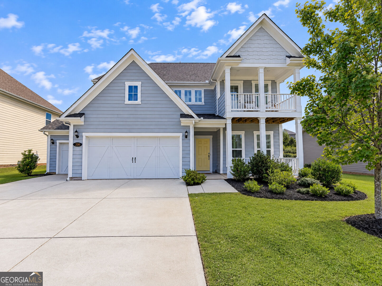 Blue-gray two-story house with white porches, double garage, yellow door, and landscaped front yard.