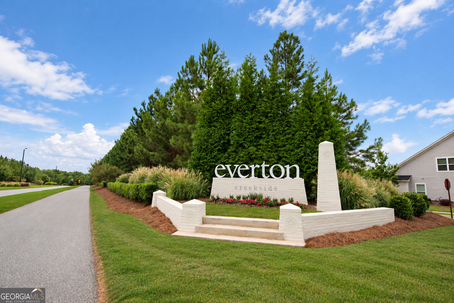 Everton Creekside entrance sign beside a landscaped road and tall trees.
