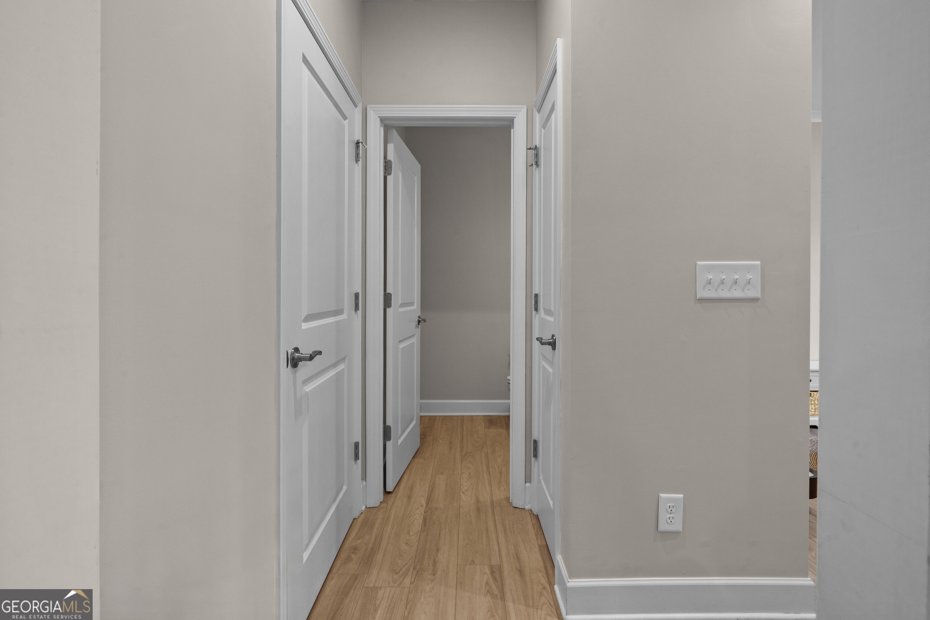 Hallway with light wood floors and several open white paneled doors.