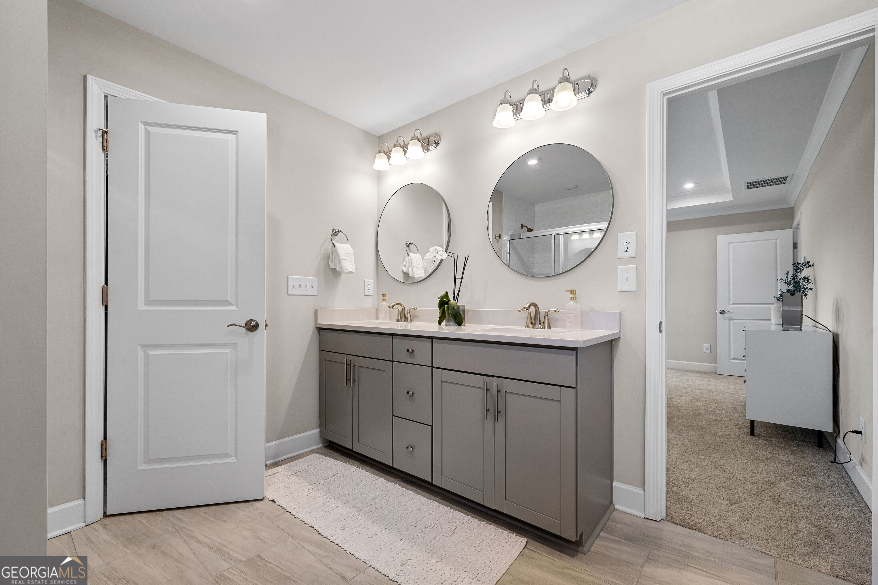 Bathroom with a gray double vanity, two round mirrors, and a glass shower reflected in the larger mirror.