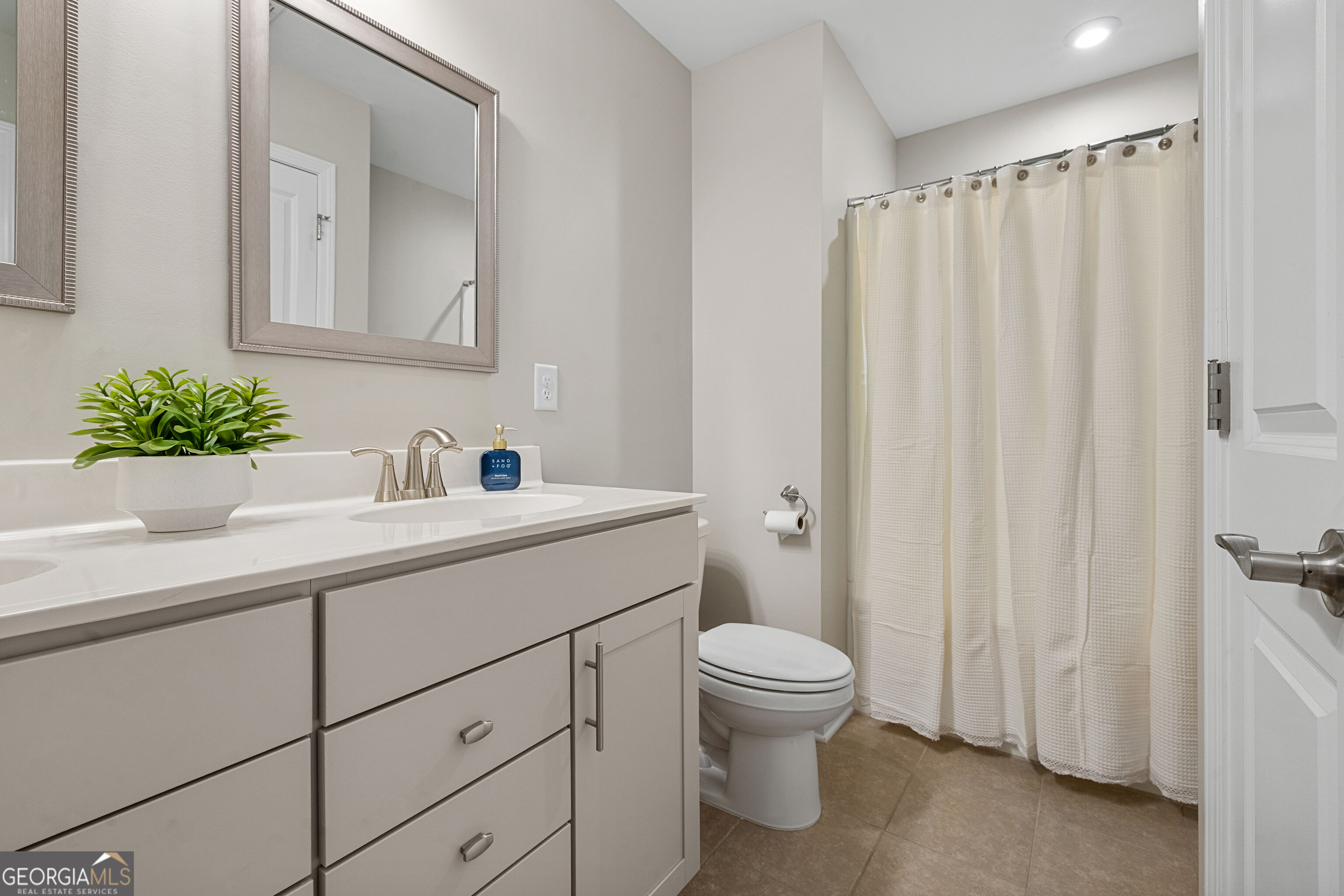 Bathroom with a white vanity, framed mirror, toilet, and cream shower curtain.