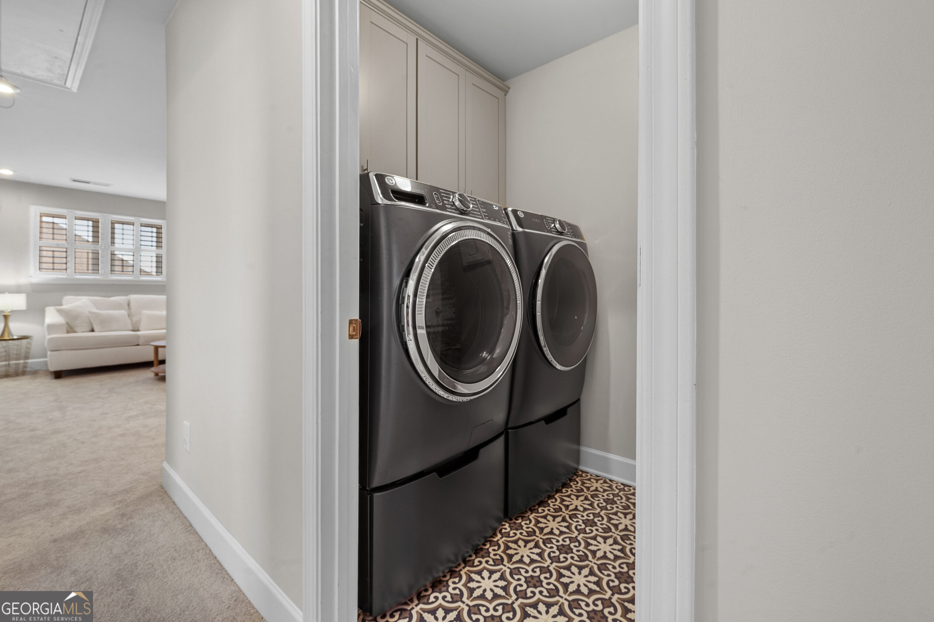 Laundry room with black front-loading washer and dryer, patterned tile floor, and cabinets.