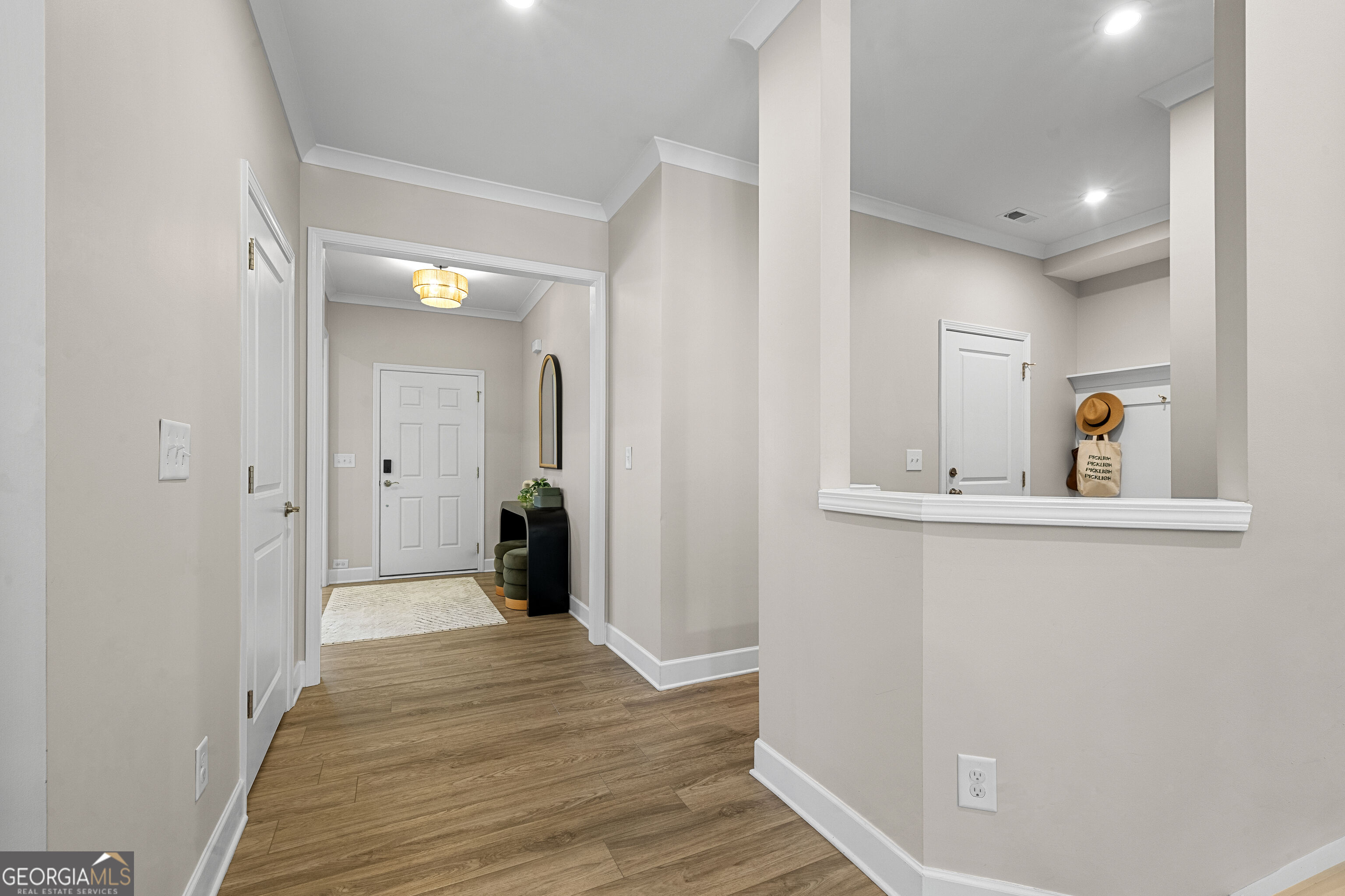 Staged entryway with wood-look floors, a white front door, and a pass-through coat nook.