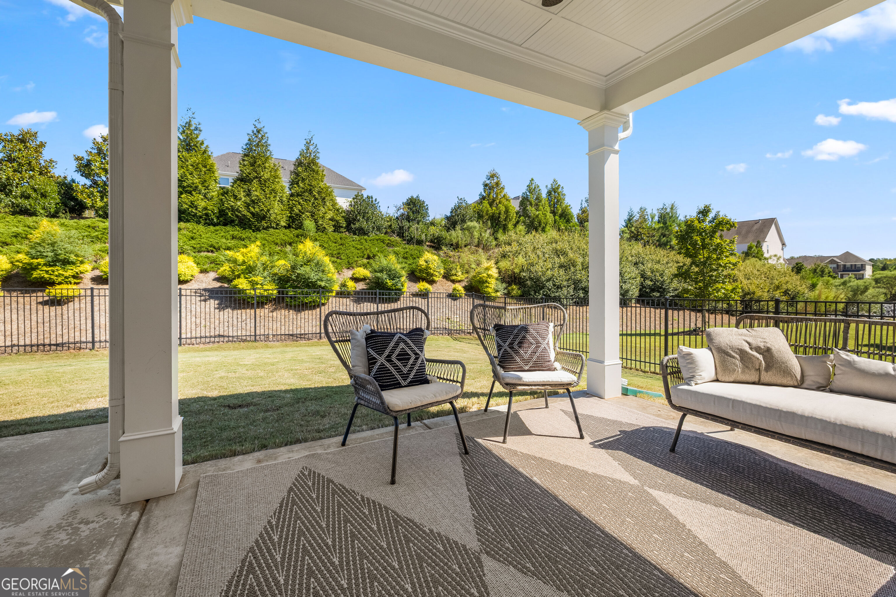 Covered back patio with wicker seating overlooking a fenced lawn and landscaped garden.