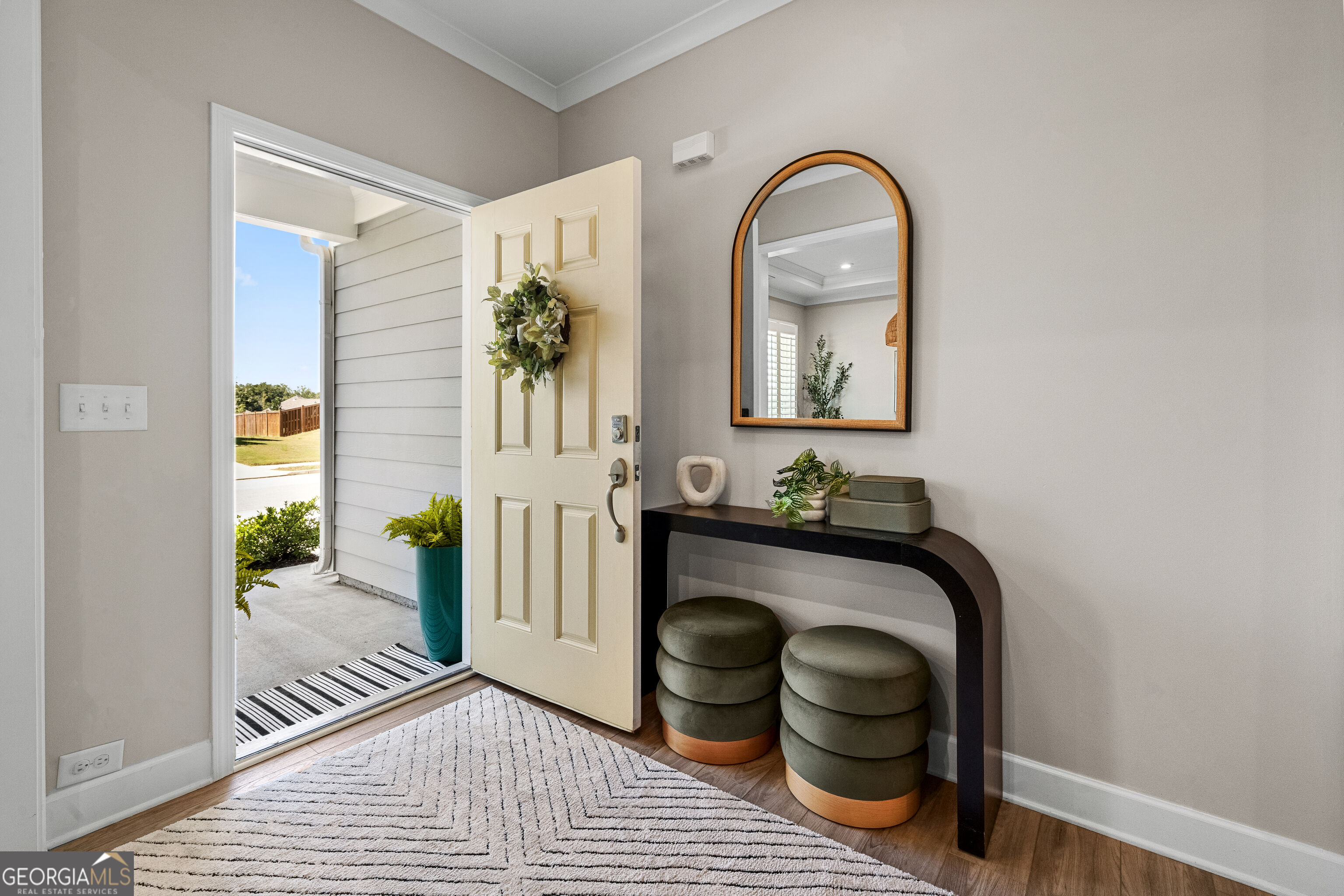 Entry foyer with an open front door, arched mirror, console table, and two round stools.