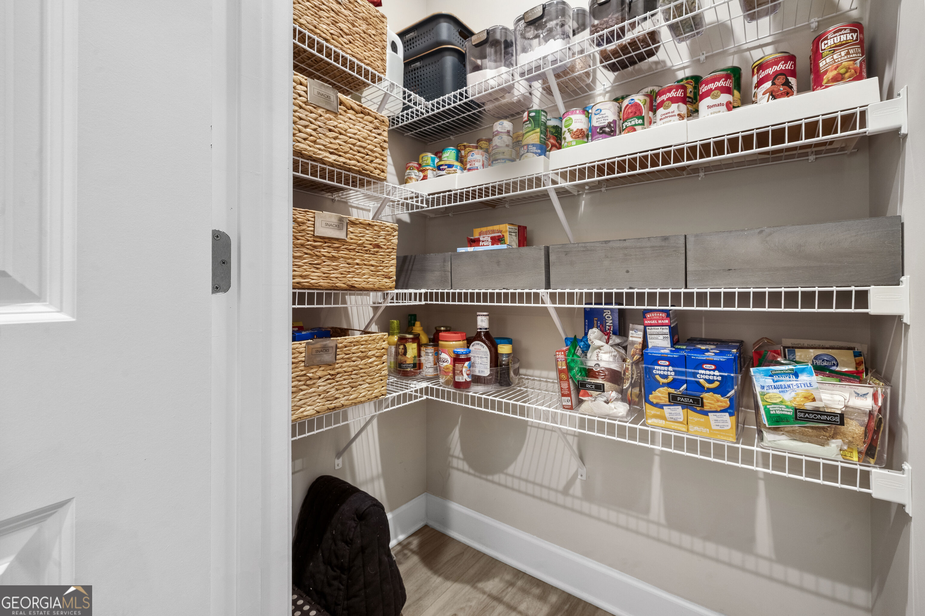 Walk-in pantry with stocked wire shelves, woven baskets, clear containers, and gray storage bins.